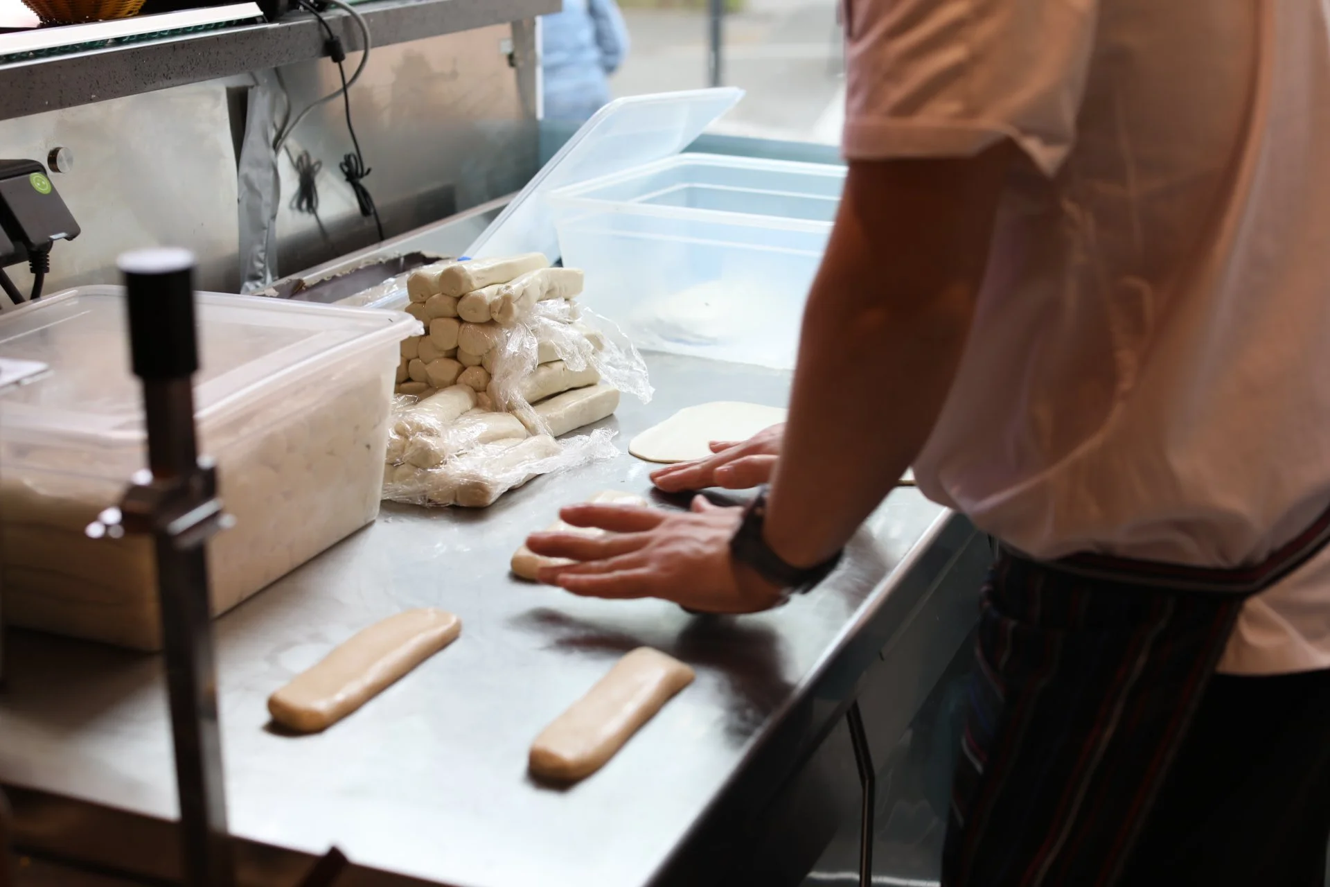 Une personne prépare des baguettes de pain dans une boulangerie, avec des pâtons de pâte à pain et des baguettes déjà façonnées sur la table.