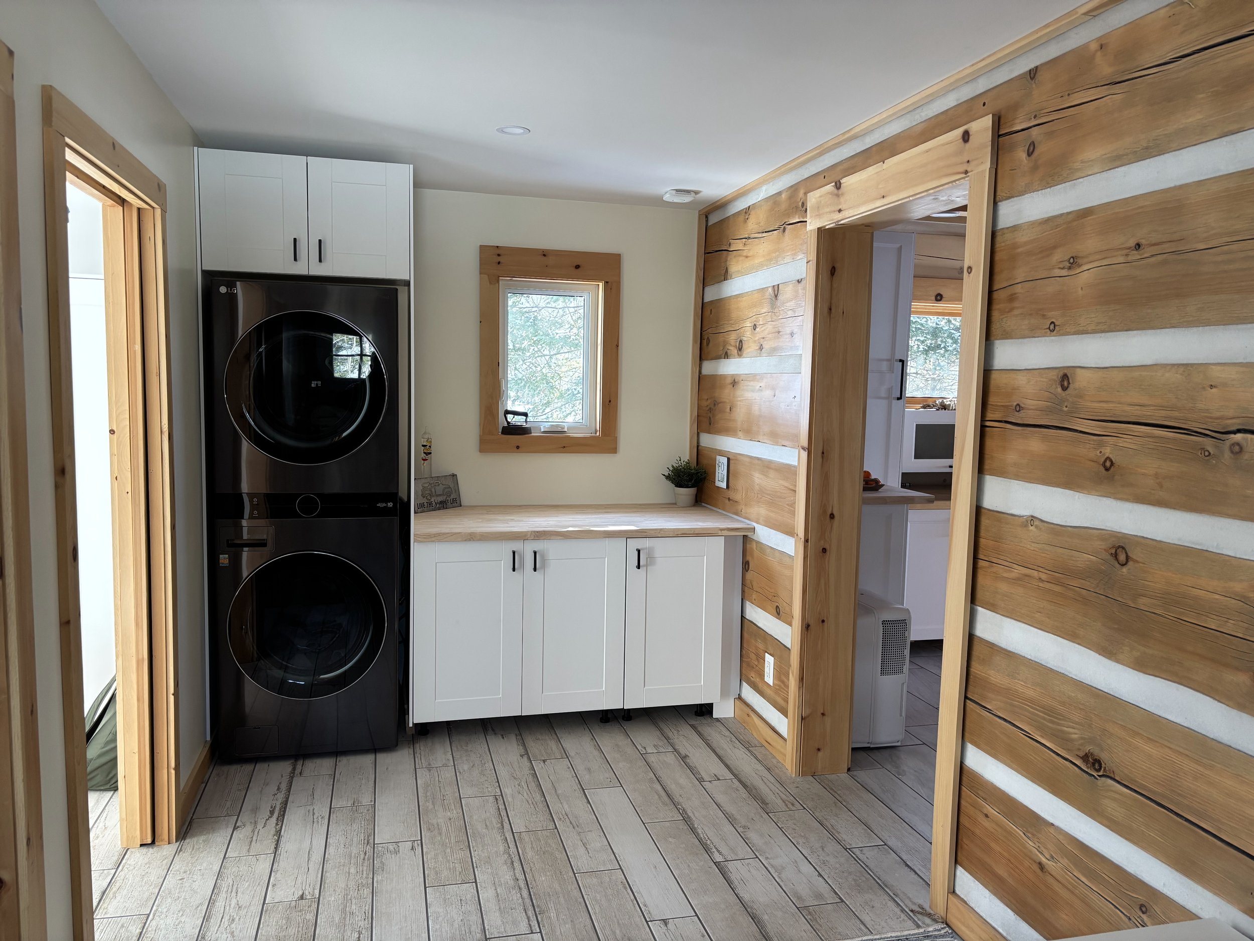 Laundry room with stacked washer and dryer, white cabinets, log cabin-style wood paneling, and tile flooring.
