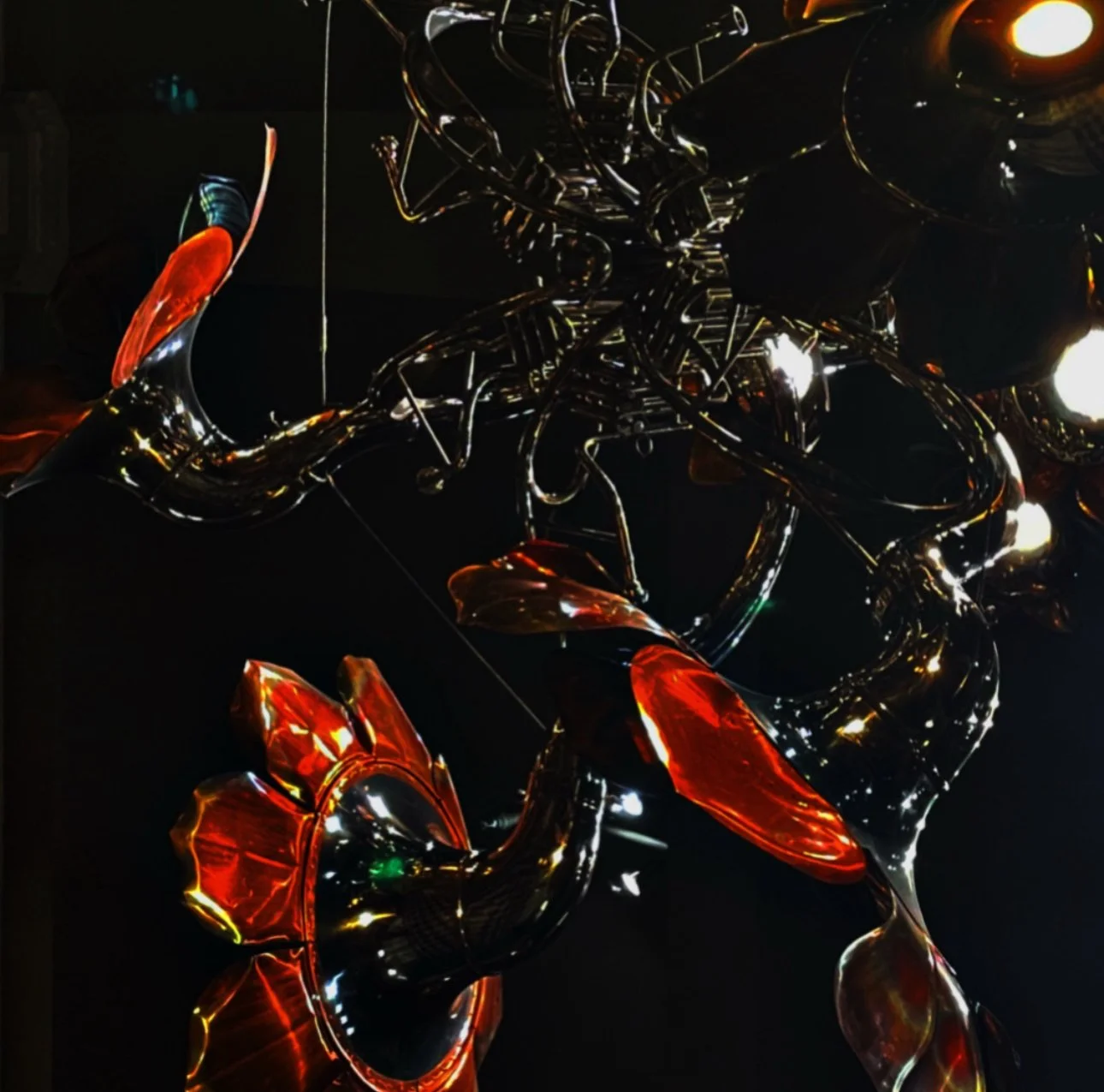 A colorful glass sculpture resembling flowers with red and black petals, set against a dark background.
