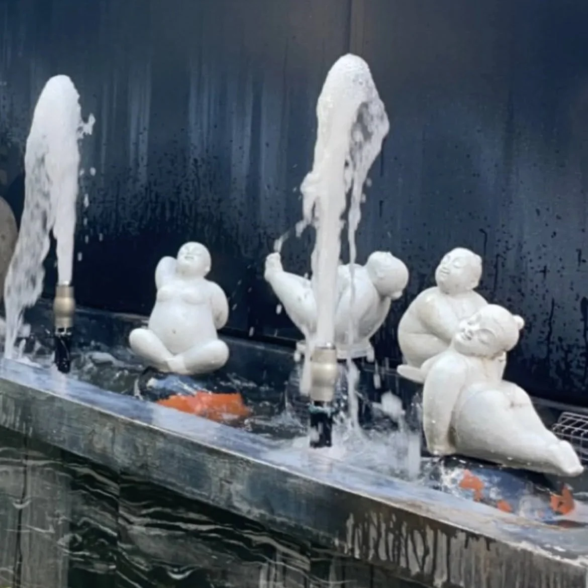 White ceramic figurines of children and duck sculptures in a water fountain display.