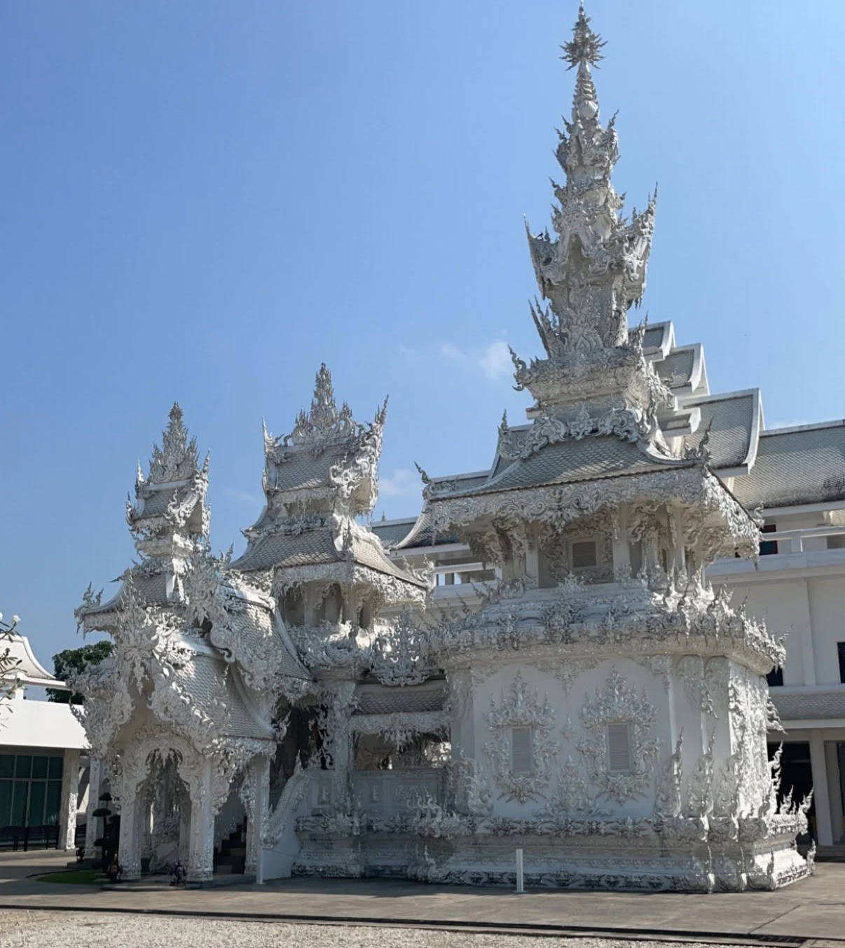 White ornate temple with intricate carvings and multiple spires, set against a clear blue sky.
