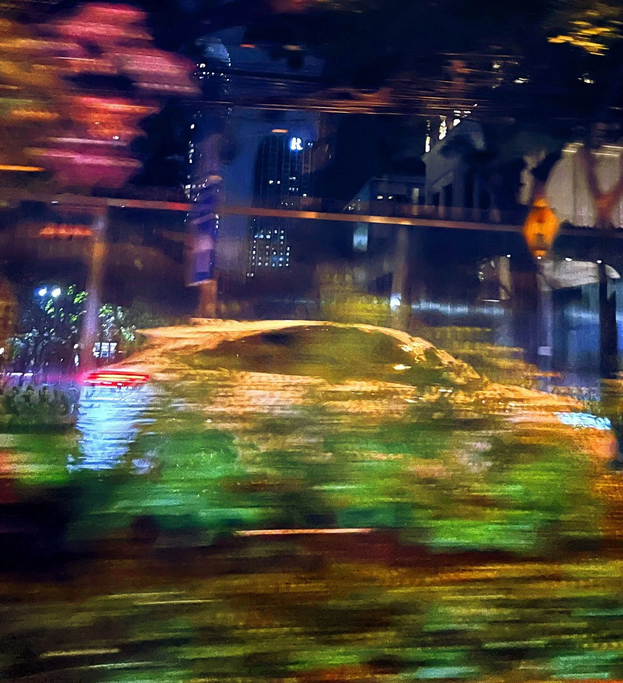 Blurred night scene with colorful lights, trees, and city buildings in the background.