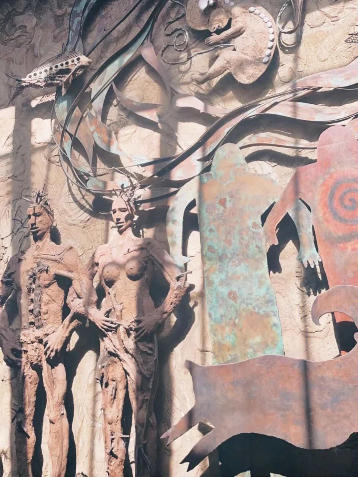 A textured wall with artistic sculptures including two human figures, a fish, and various abstract shapes and objects.