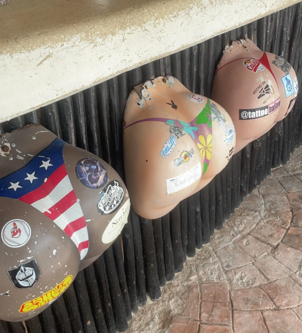 Four decorative egg-shaped objects with various stickers and paint, placed upside down on a black slatted surface.