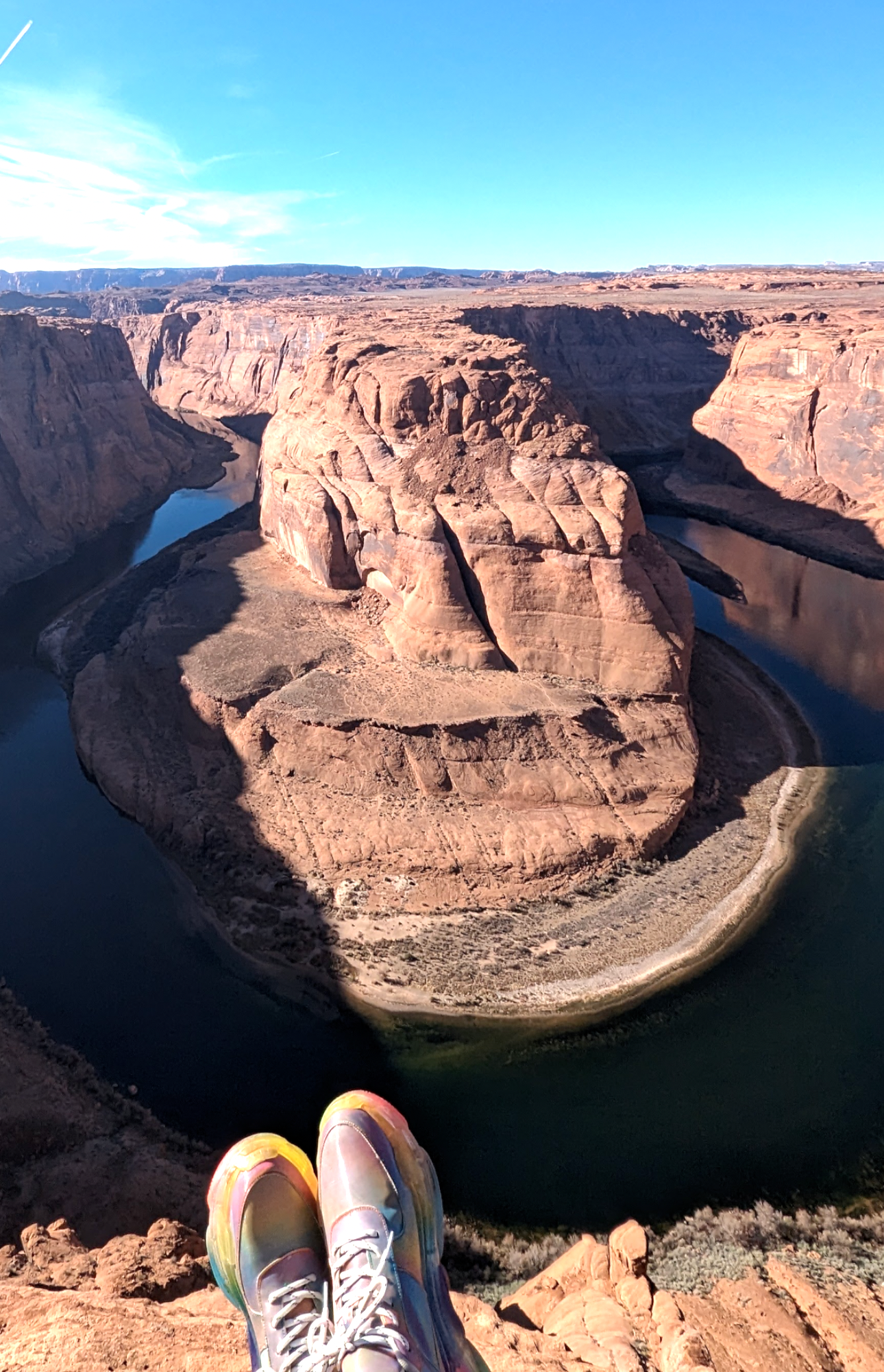 View of Horseshoe Bend on the Colorado River in Arizona, with person's colorful sneakers visible at the edge of the cliff.