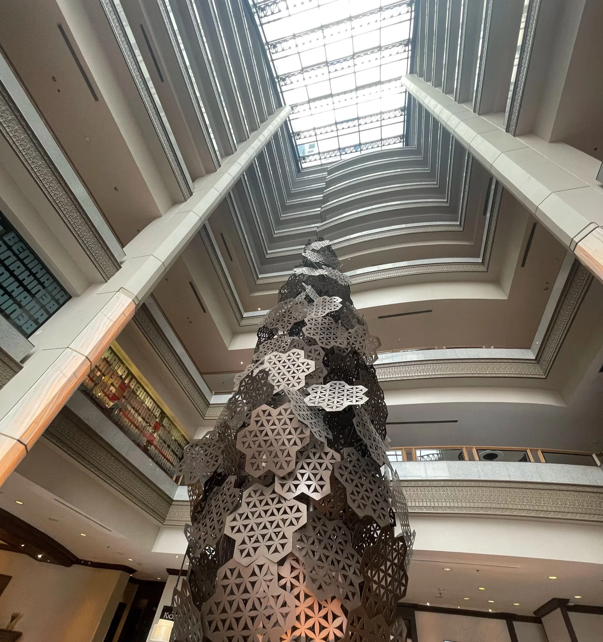 Interior view of a multi-story hotel lobby with a modern abstract sculpture reaching towards the ceiling, with skylights above.