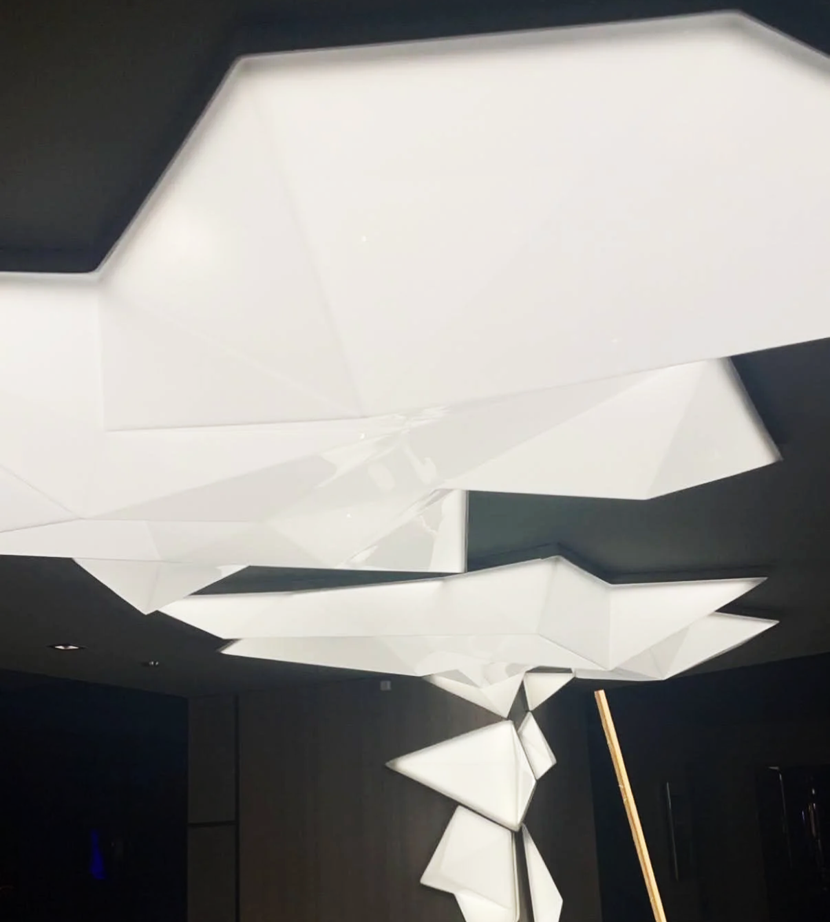 Modern geometric white ceiling lights with angular shapes hanging in a dark room.