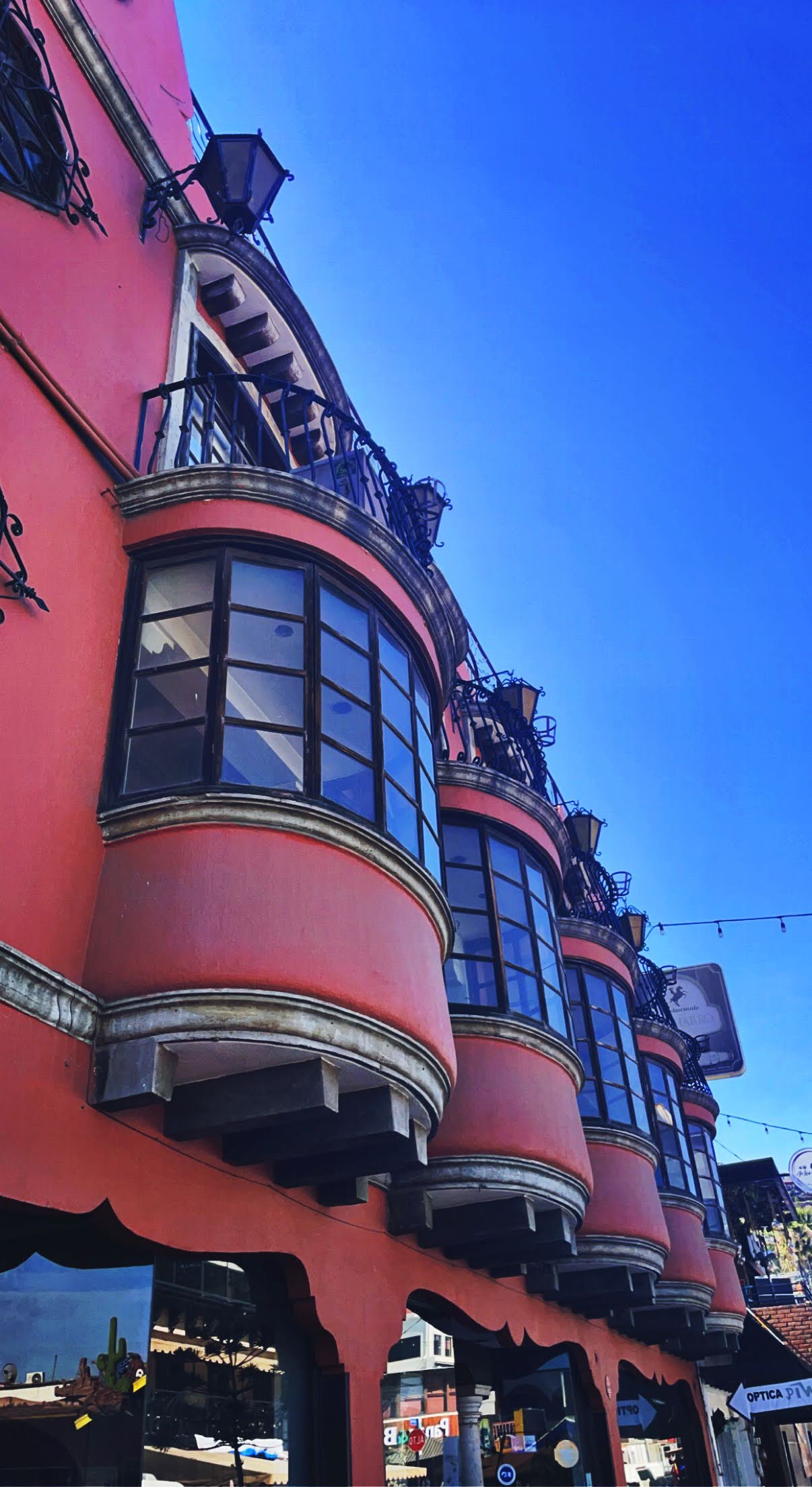 Pink building with rounded bay windows and iron balconies, against a clear blue sky.