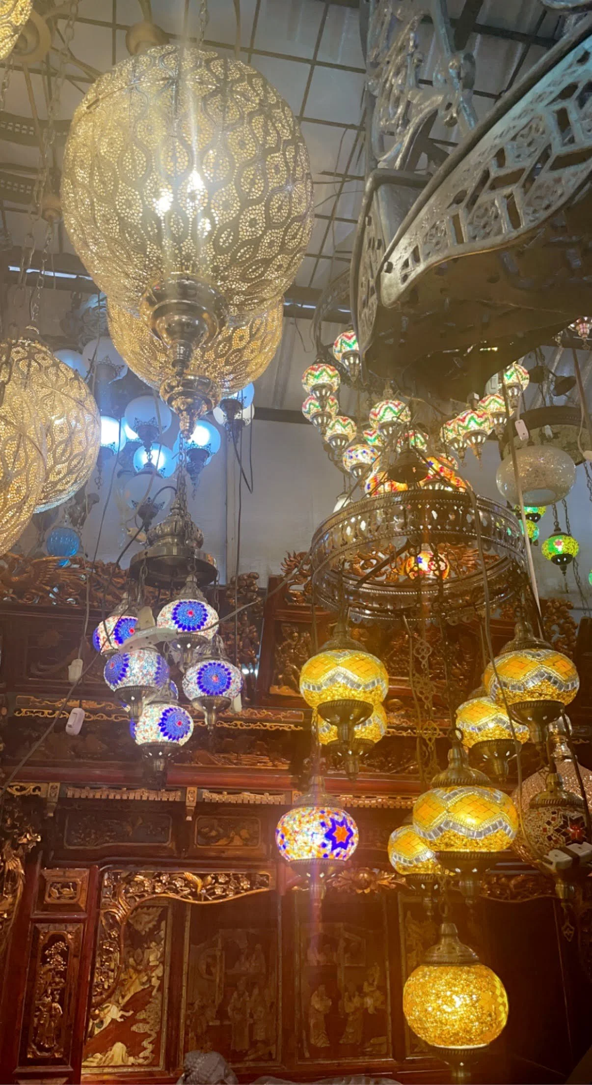 A display of various decorative hanging lamps and lanterns in different shapes, sizes, and colors, including intricate patterns, in a lighting or decor shop.