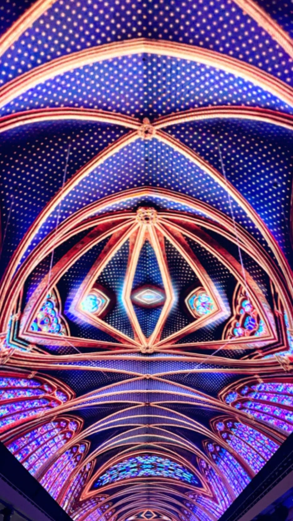 Colorful illuminated ceiling of a cathedral with intricate gothic patterns and stained glass windows.