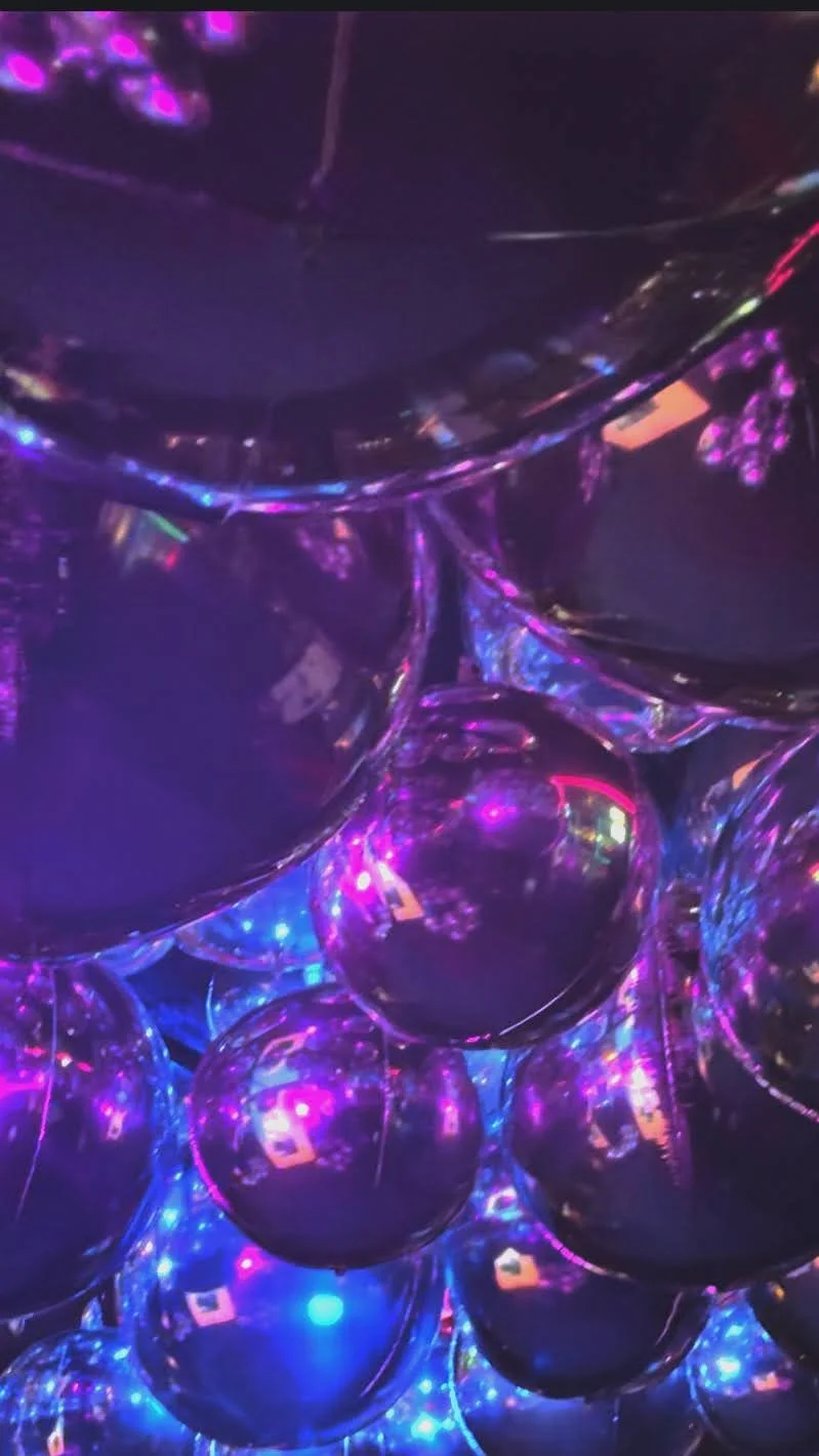 A bunch of shiny, metallic purple balloons illuminated by multicolored LED lights, creating a vibrant, festive atmosphere.