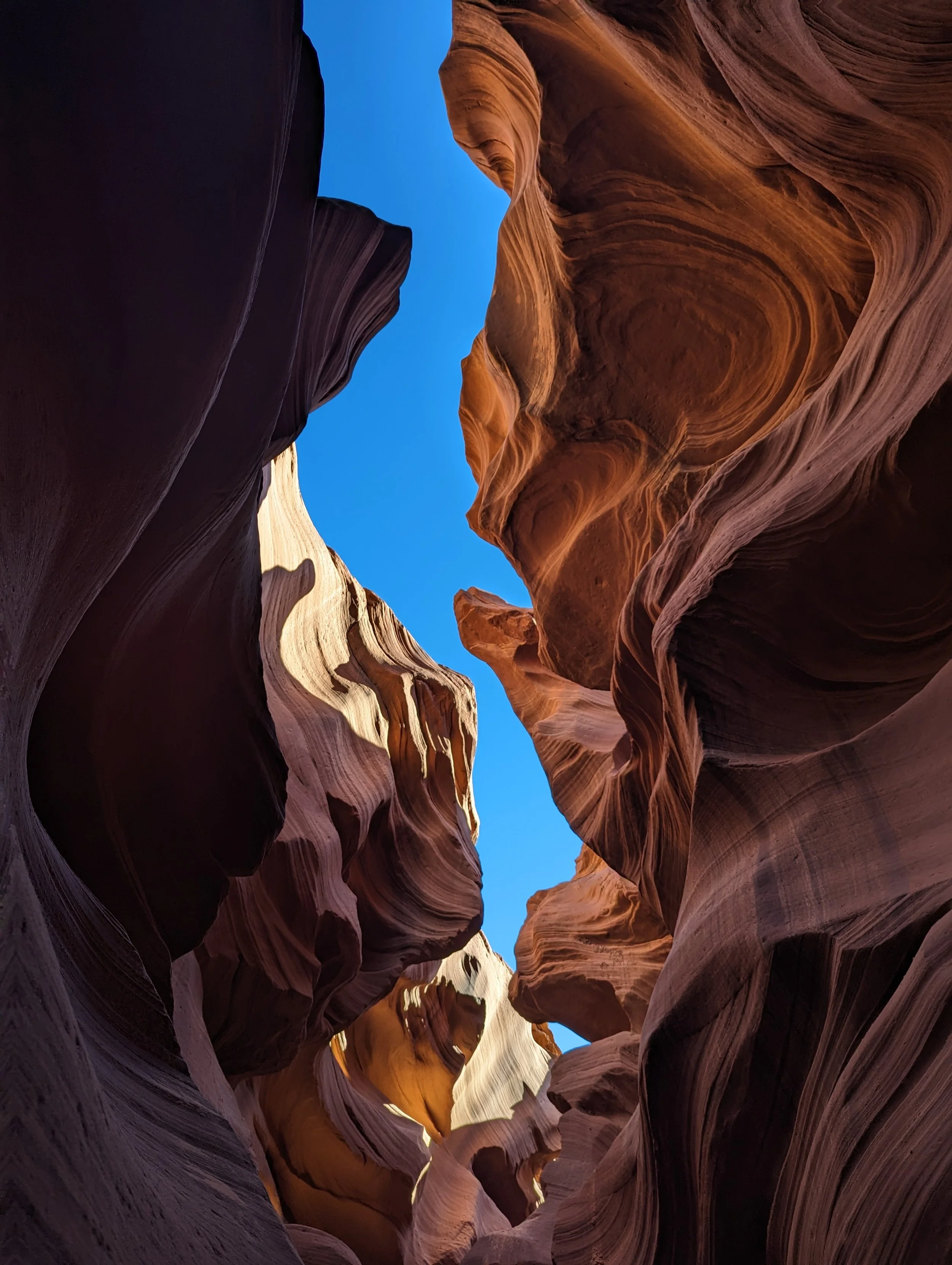 View of a narrow slot canyon with undulating sandstone walls and a bright blue sky visible at the top.