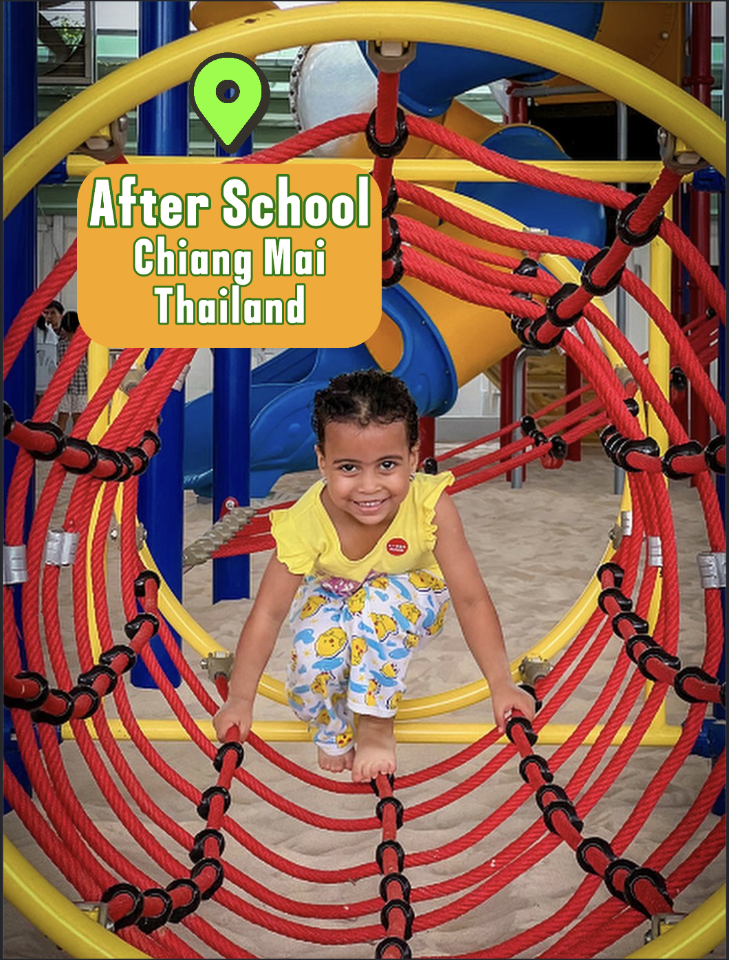 Bambina sorridente che si arrampica su una struttura da gioco colorata con scivolo e corde rosse, in un parco giochi all'aperto in Thailandia