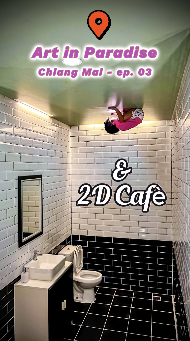 Interno di un bagno con pareti di piastrelle bianche e nere, un lavabo con specchio e un water. Sopra, un bambino con una maglietta rosa e pantaloni verdi, seduto a testa in giù. Sopra, il testo 'Art in Paradise Chiang Mai - ep. 03' e ' & 2D Café'.