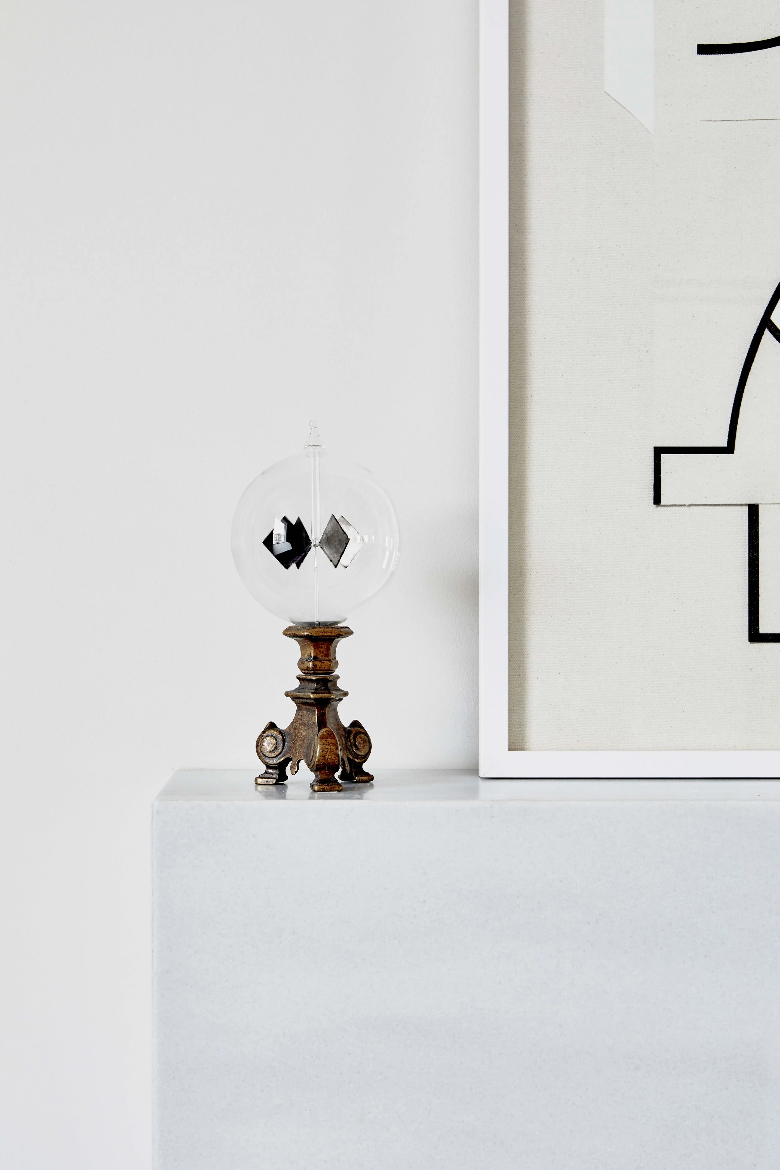 Decorative glass object with a metal base on a white surface next to framed artwork.