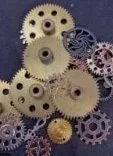 A collection of various gears and cogs in different sizes, colors, and designs arranged against a dark background.