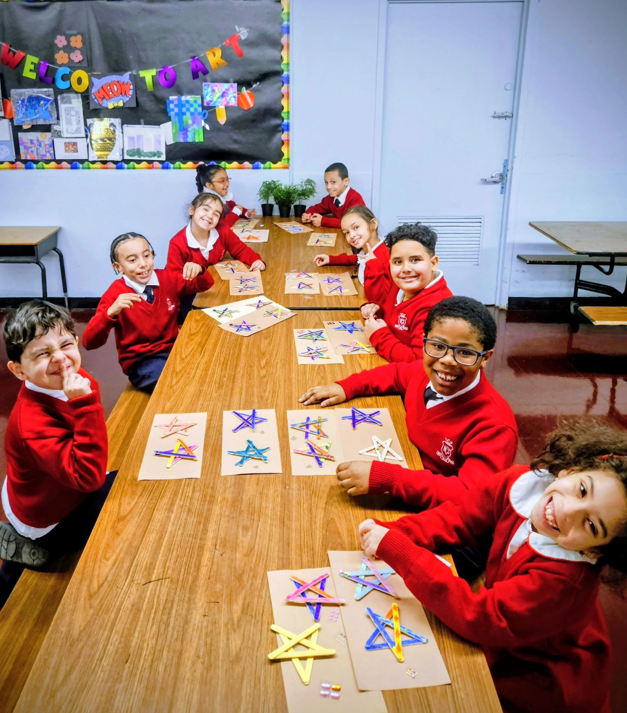 kids in uniform at school doing an art project at a long wooden table smiling