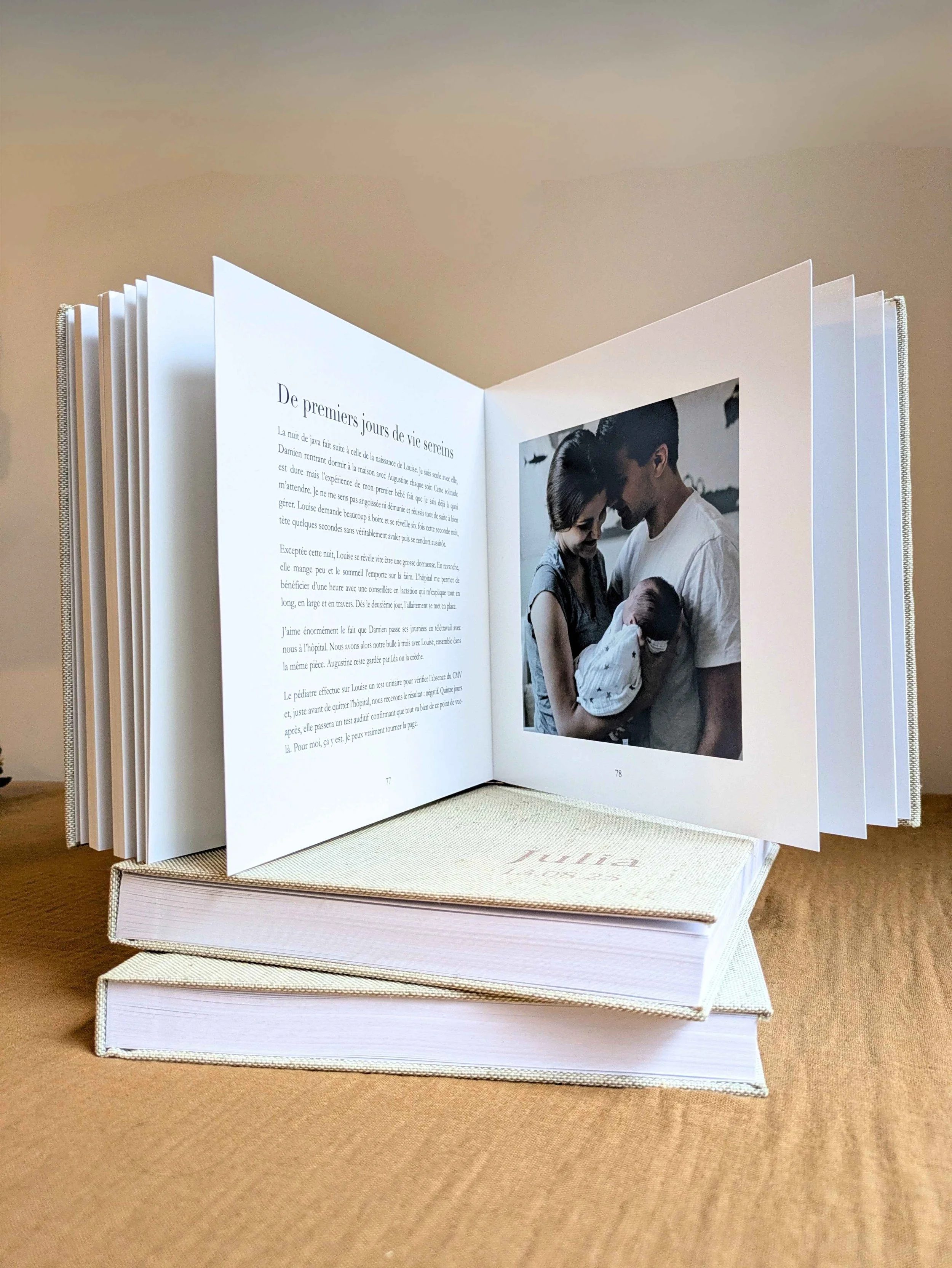 L'image représente un livre ouvert de récit de naissance ou récit d'adoption posé sur d'autres livres souvenirs  à la couverture rigide en tissu et aux pages épaisses.