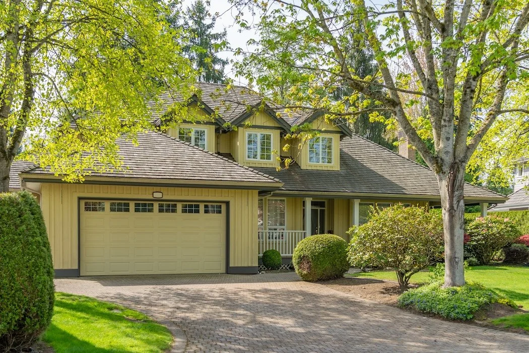 Yellow Home with multiple trees in the front yard with spring growth