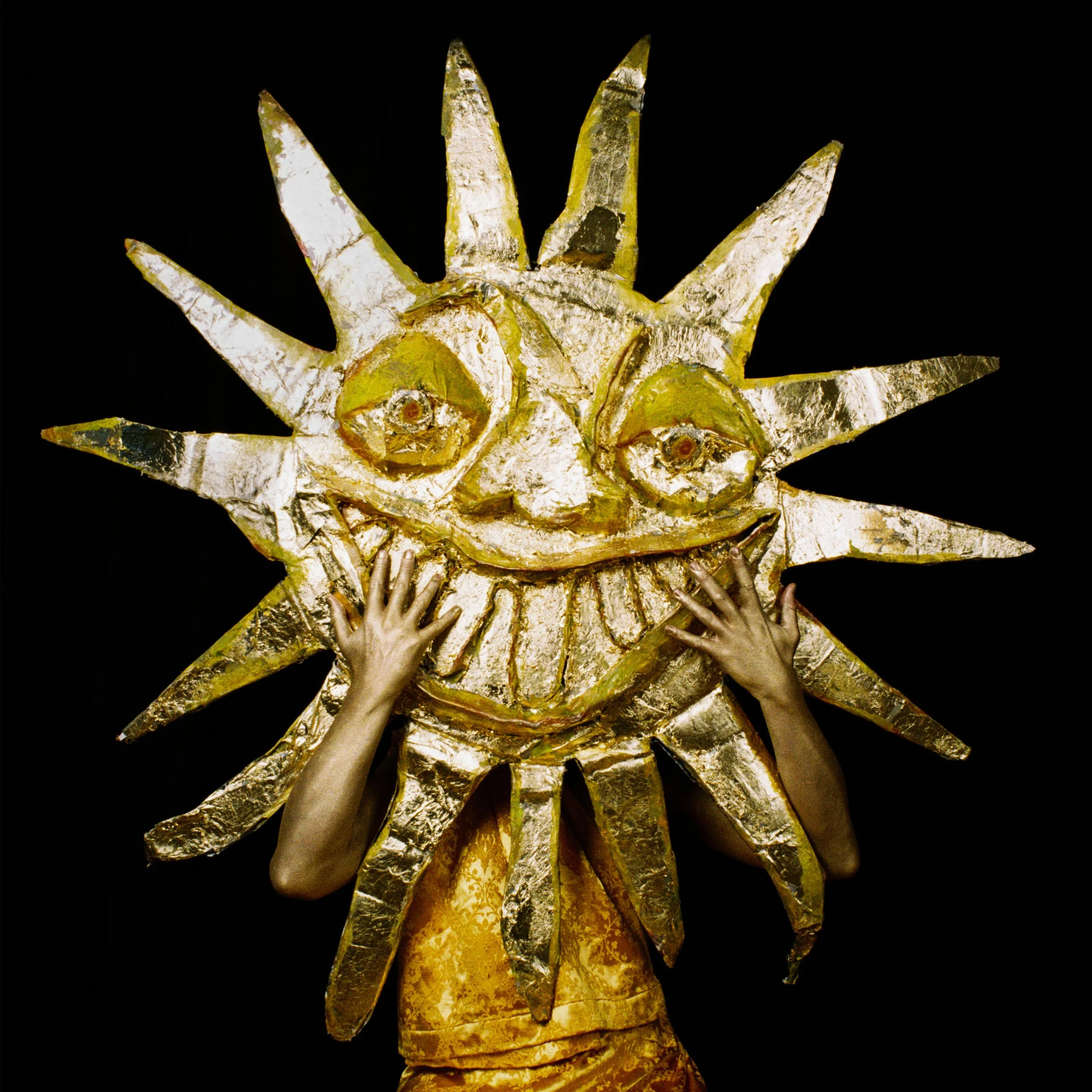 The album art for Peter Cat's Starchamber album, showing a person wearing a golden costume with a large sun-shaped mask featuring a smiling face, with arms reaching up toward the mask.