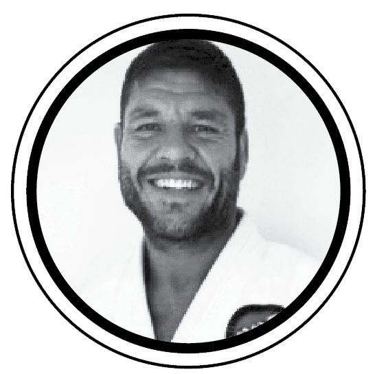 A black and white headshot of a smiling man with short hair and a beard, wearing a martial arts uniform.