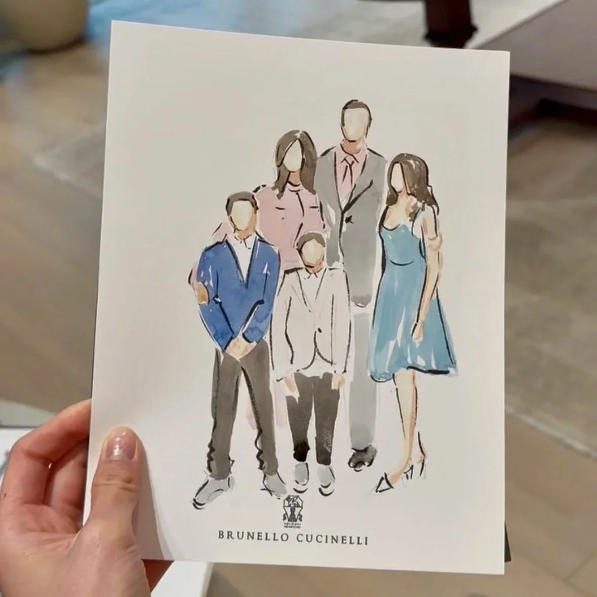 A watercolor illustration of a family of five people dressed in formal attire, with three adults and two children, posing together. The illustration is signed by Brunello Cucinelli.
