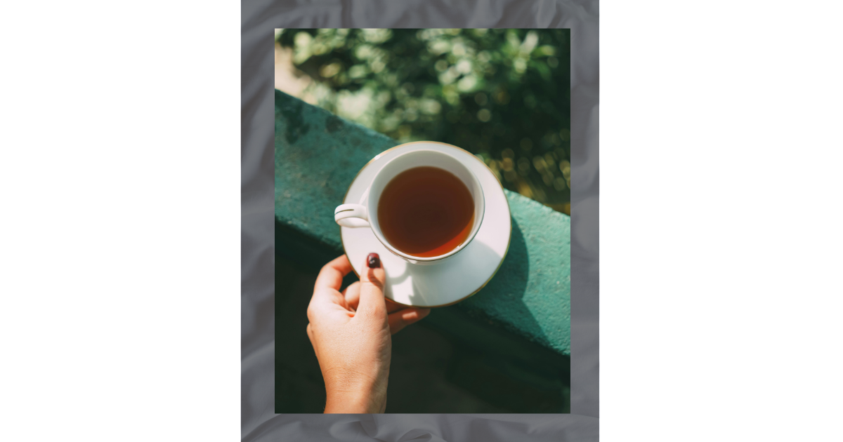 Hand holding a white teacup on a balcony, capturing a quiet moment of self-care or morning ritual.