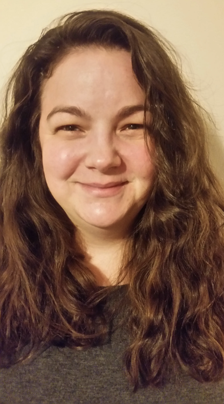 Smiling person with long brown hair wearing a dark shirt.