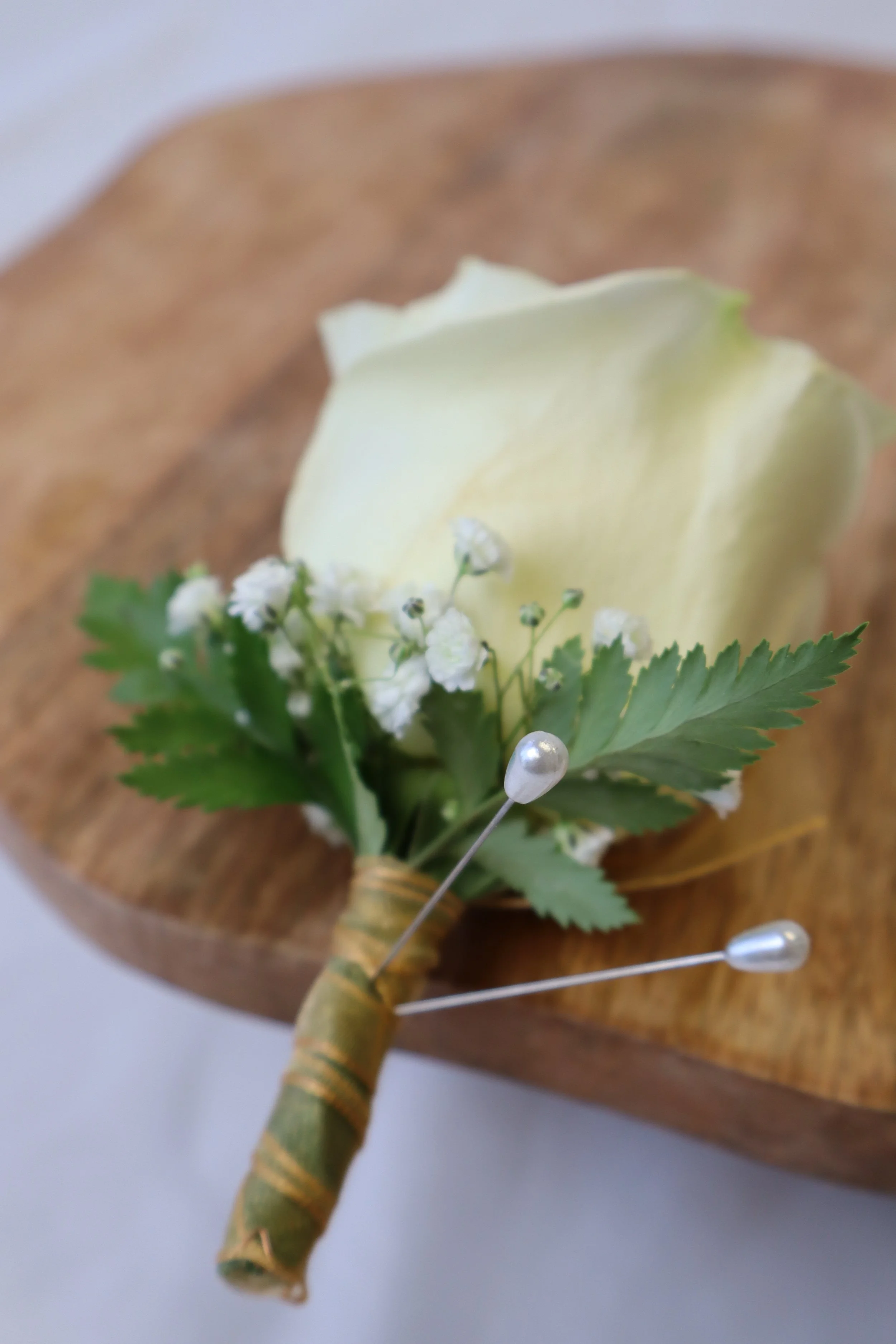 Prom rose boutonniere with white rose, greenery, and pins on wood surface