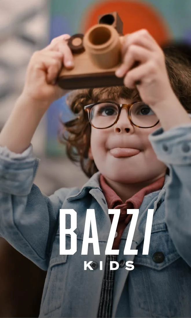 Niño con gafas sosteniendo un juguete de control remoto, haciendo una expresión divertida con la lengua afuera, en un ambiente colorido.