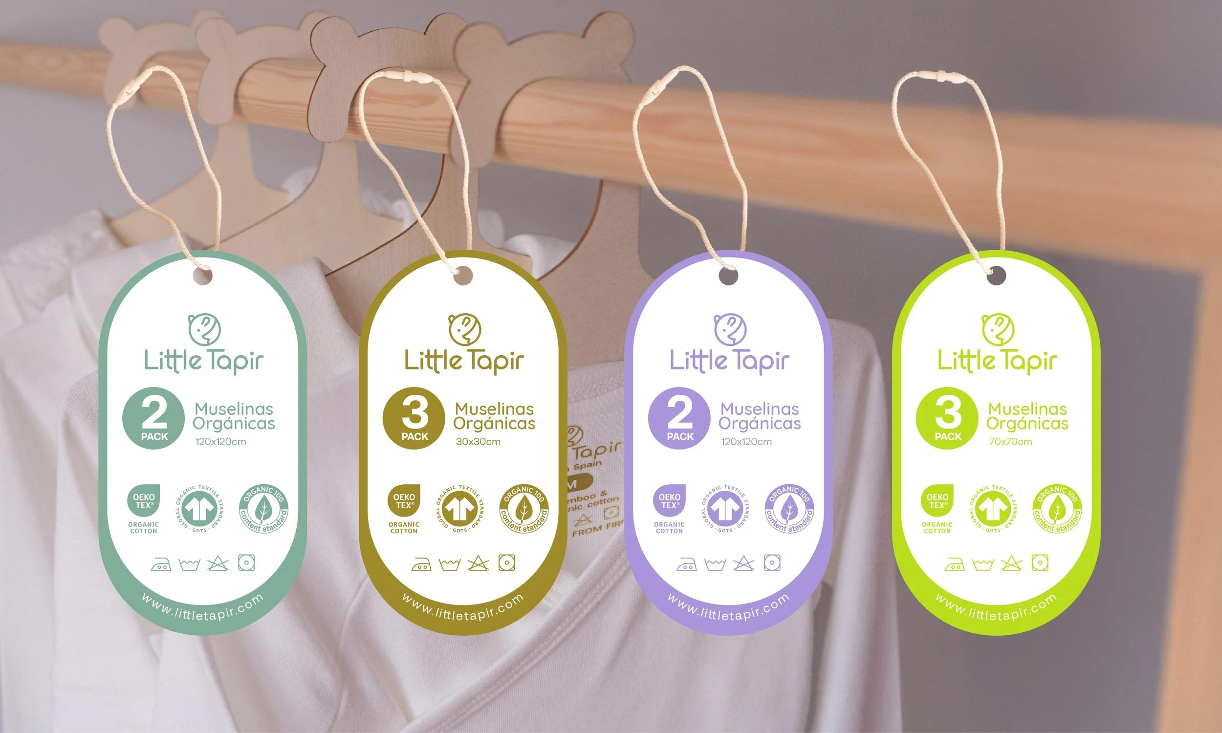 Etiquetas colgadas de perchas que contienen información sobre muselinas orgánicas de la marca Little Tapir en diferentes tamaños y cantidades, con íconos y detalles en colores variados