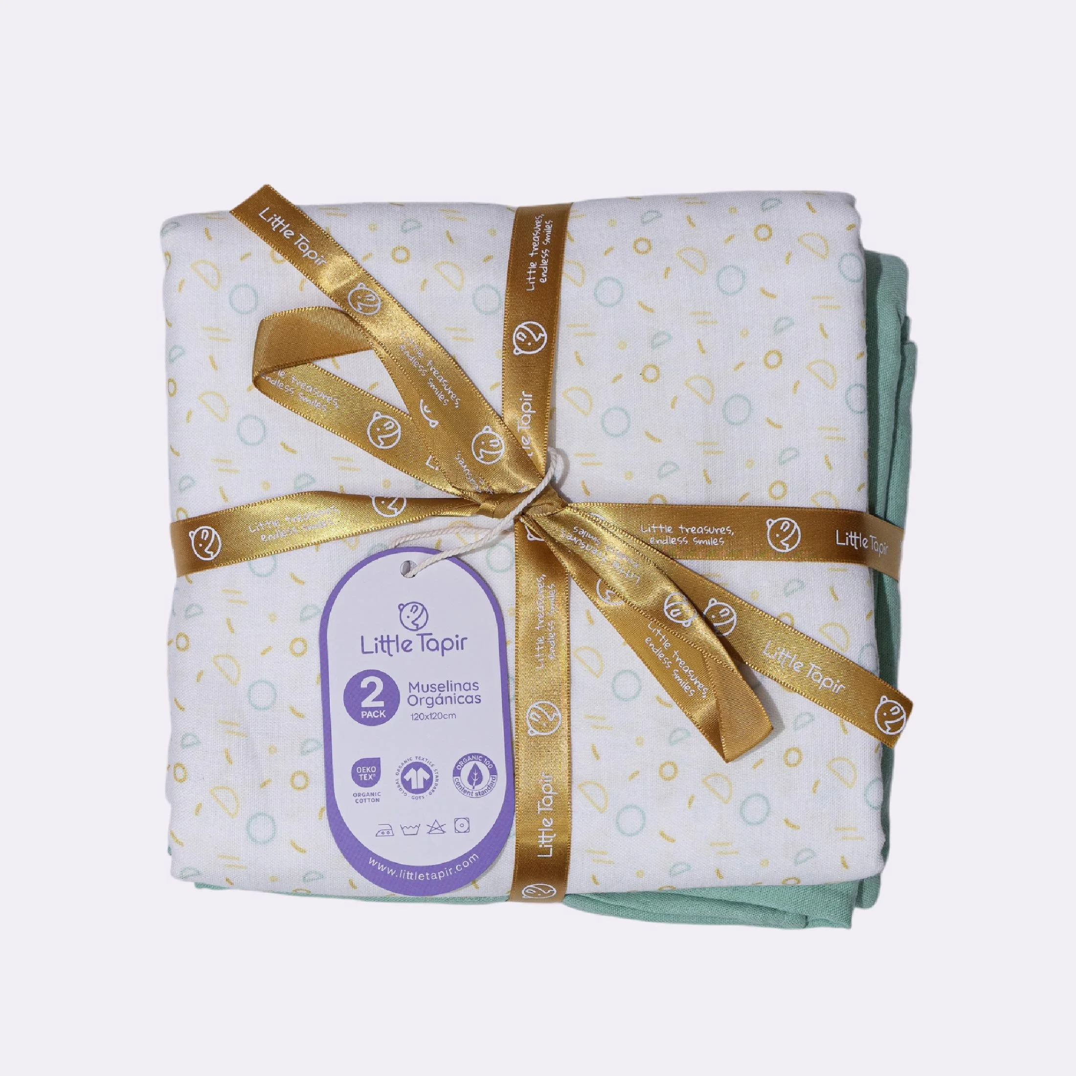 Paquete de dos muselinas orgánicas de color blanco con diseño de formas en tonos suaves, atado con cinta dorada con logotipo y mensaje, etiqueta que indica que son productos ecológicos estándar Oeko-Tex, aptas para bebés.