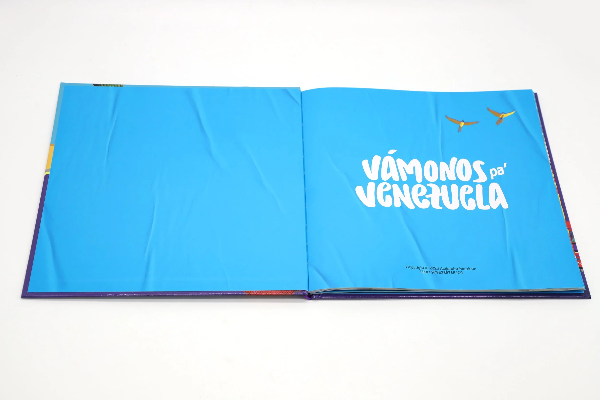 Página de un libro con fondo azul y texto en español que dice 'VÁMONOS pa' VENEZUELA', y dos aves volando en la esquina superior derecha.