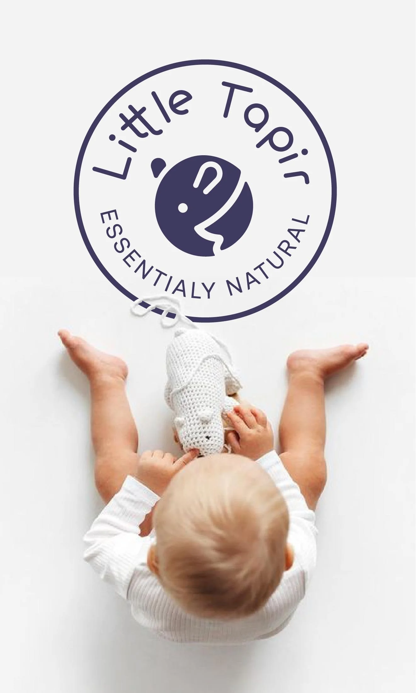 Bebé visto desde atrás, sentado en un suelo blanco, con los brazos extendidos y sosteniendo un muñeco. Encima, en el suelo, visible en la parte superior de la imagen, un logotipo de Little Tair que dice 'Essentially Natural' y tiene un dibujo de una