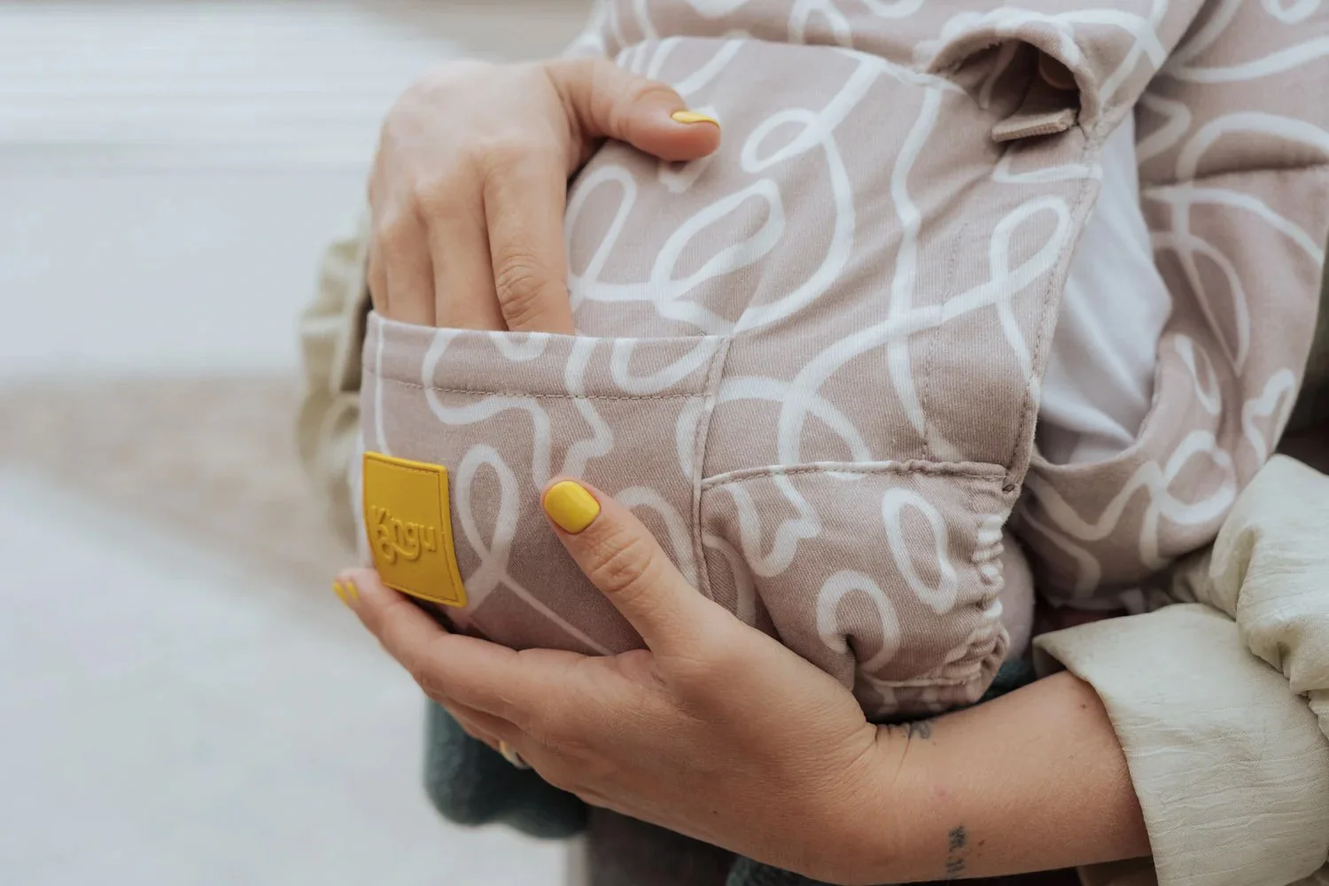 Mano sosteniendo una bolsa de tela rosa con patrón de lazo blanco, con la etiqueta amarilla de Kayu, y uñas pintadas de amarillo.