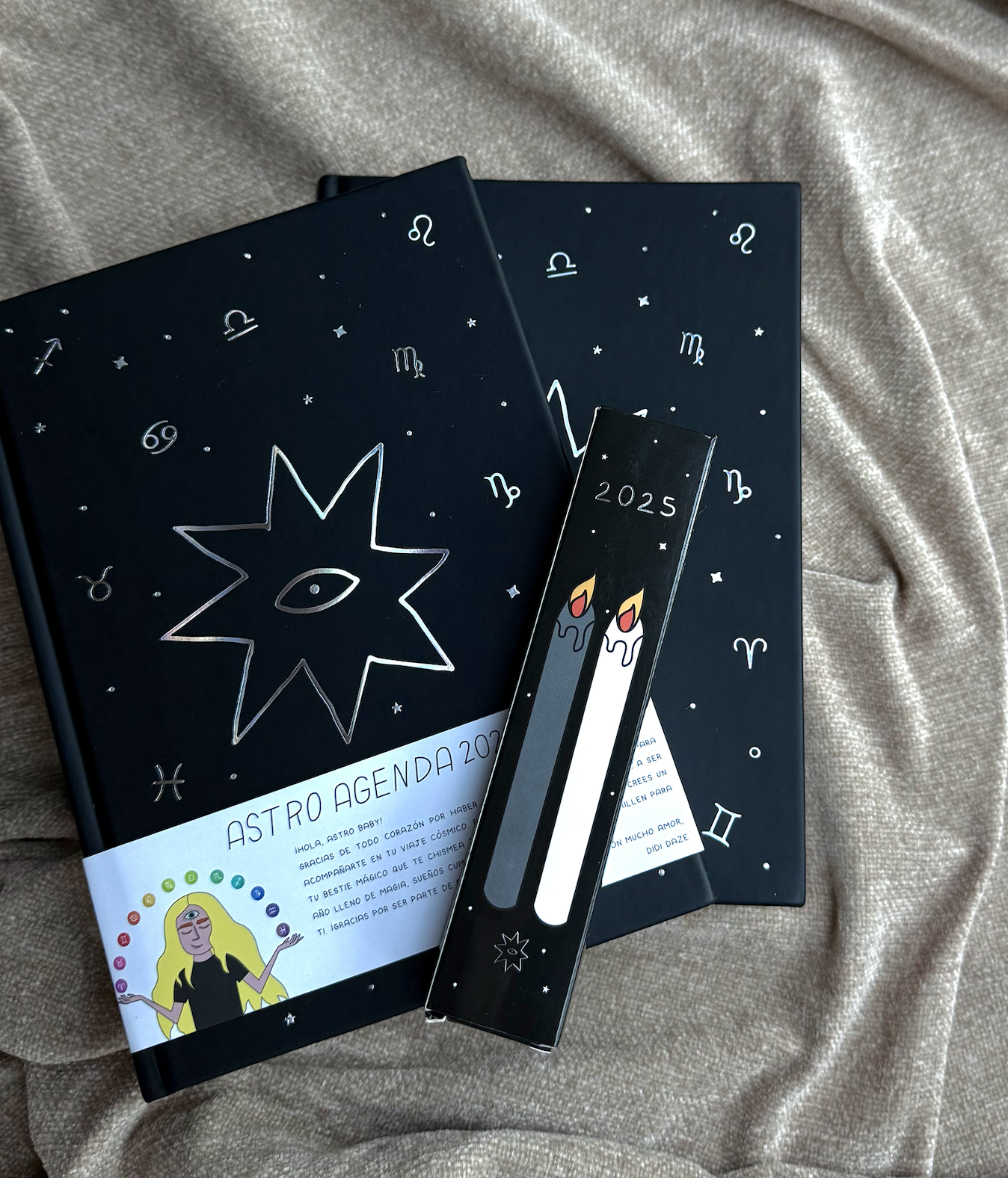 Agenda 2023 con diseño de astros y símbolos zodiacales y una vela en la cubierta, colocada sobre una tela gruesa de color beige.