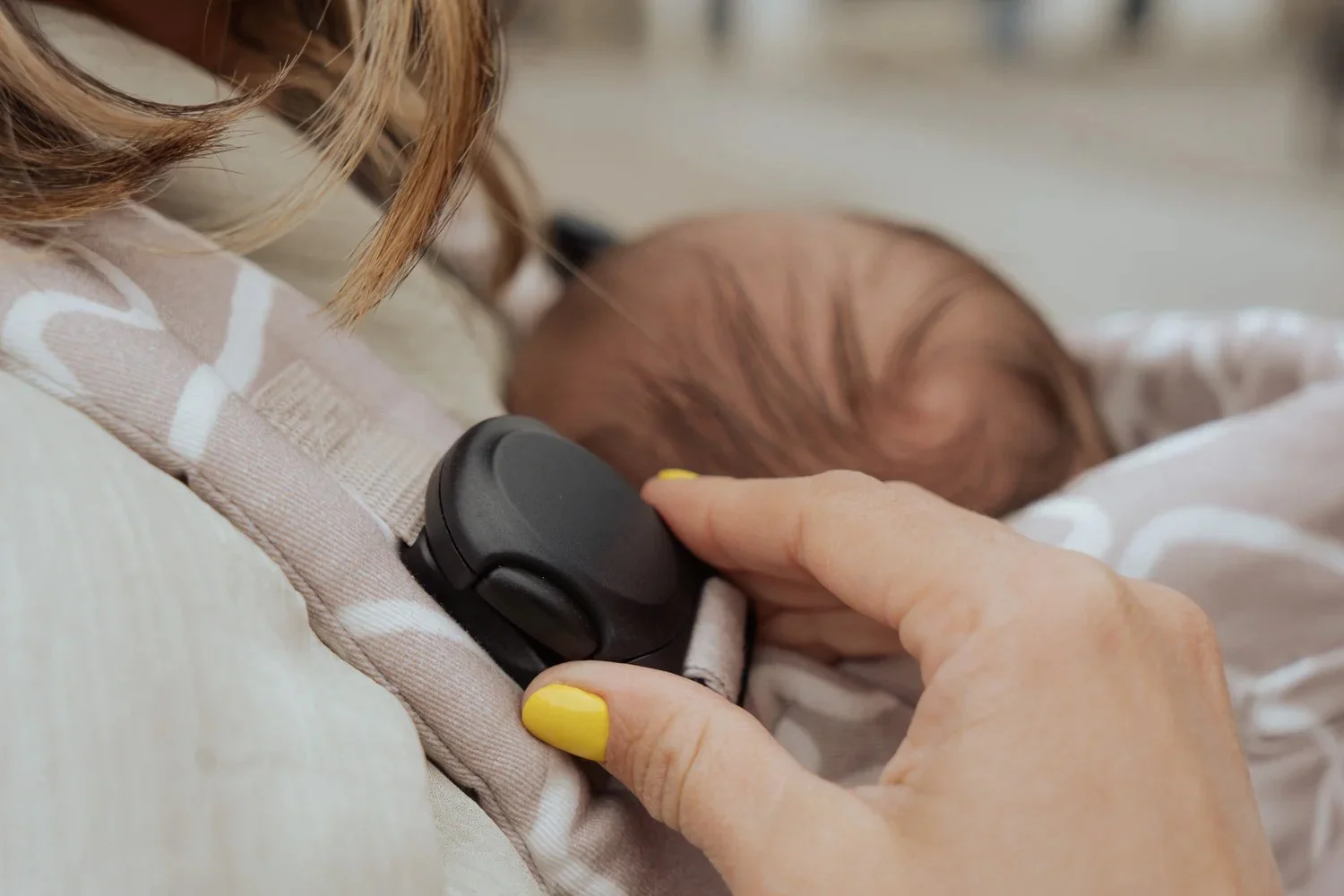 Una persona con uñas amarillas sosteniendo el monitor de ritmo cardíaco unido a un bebé que está dormido.