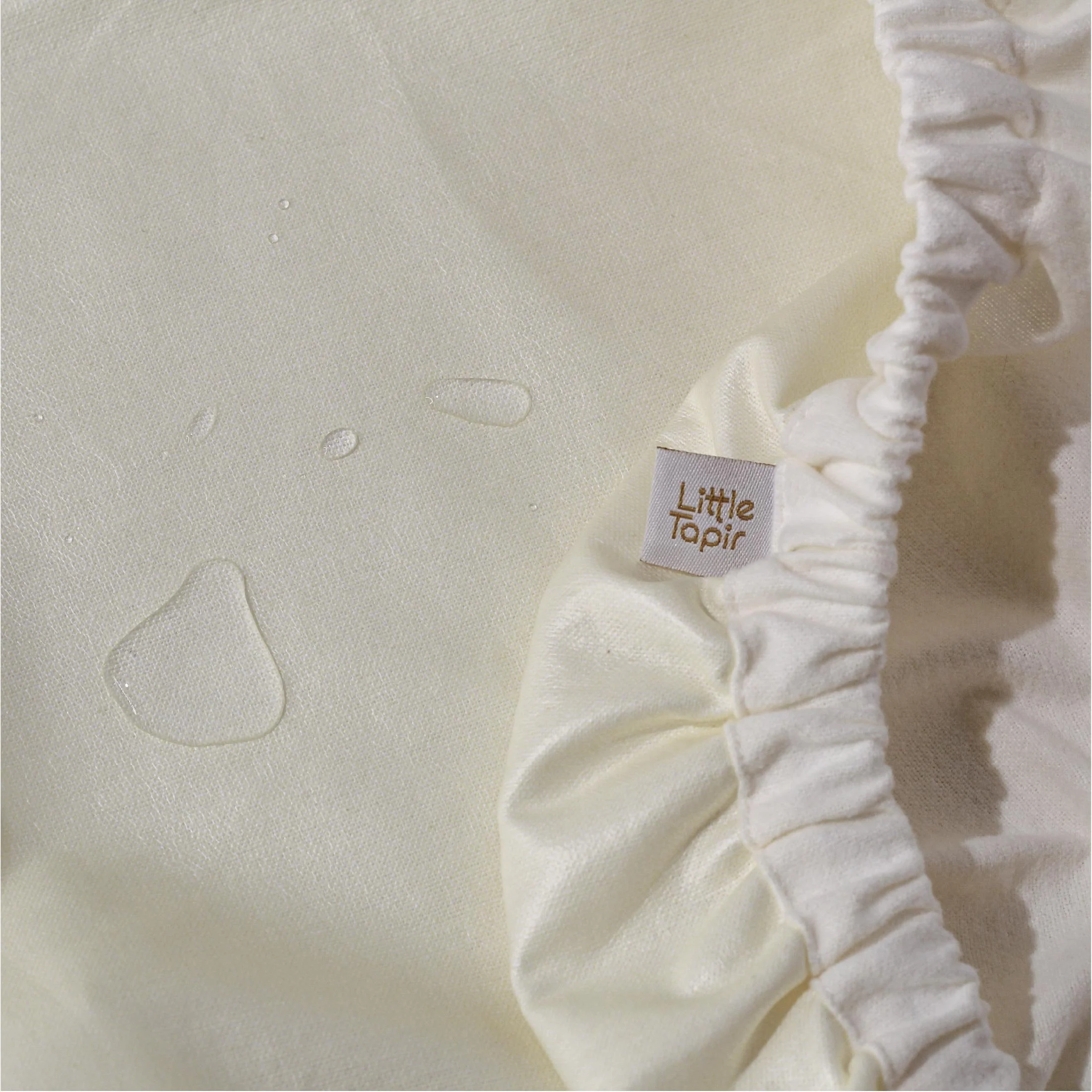 Tela blanca con gotas de agua y etiqueta que dice 'Little Tapir' junto a un dobladillo con elástico.