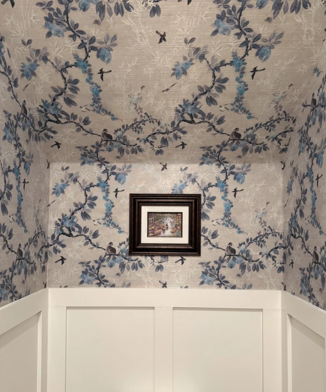 Interior wall with floral and bird patterned wallpaper, a small framed painting in the center, and white wainscoting. Spoonflower grasscloth wallpaper in belle meade Nashville.