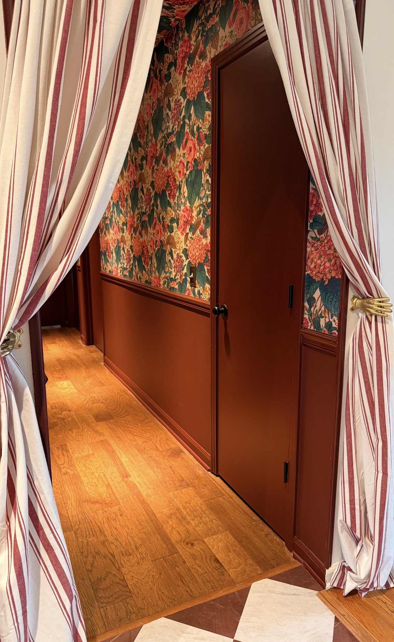 A doorway with floral wallpaper, wooden paneling, and striped curtains.