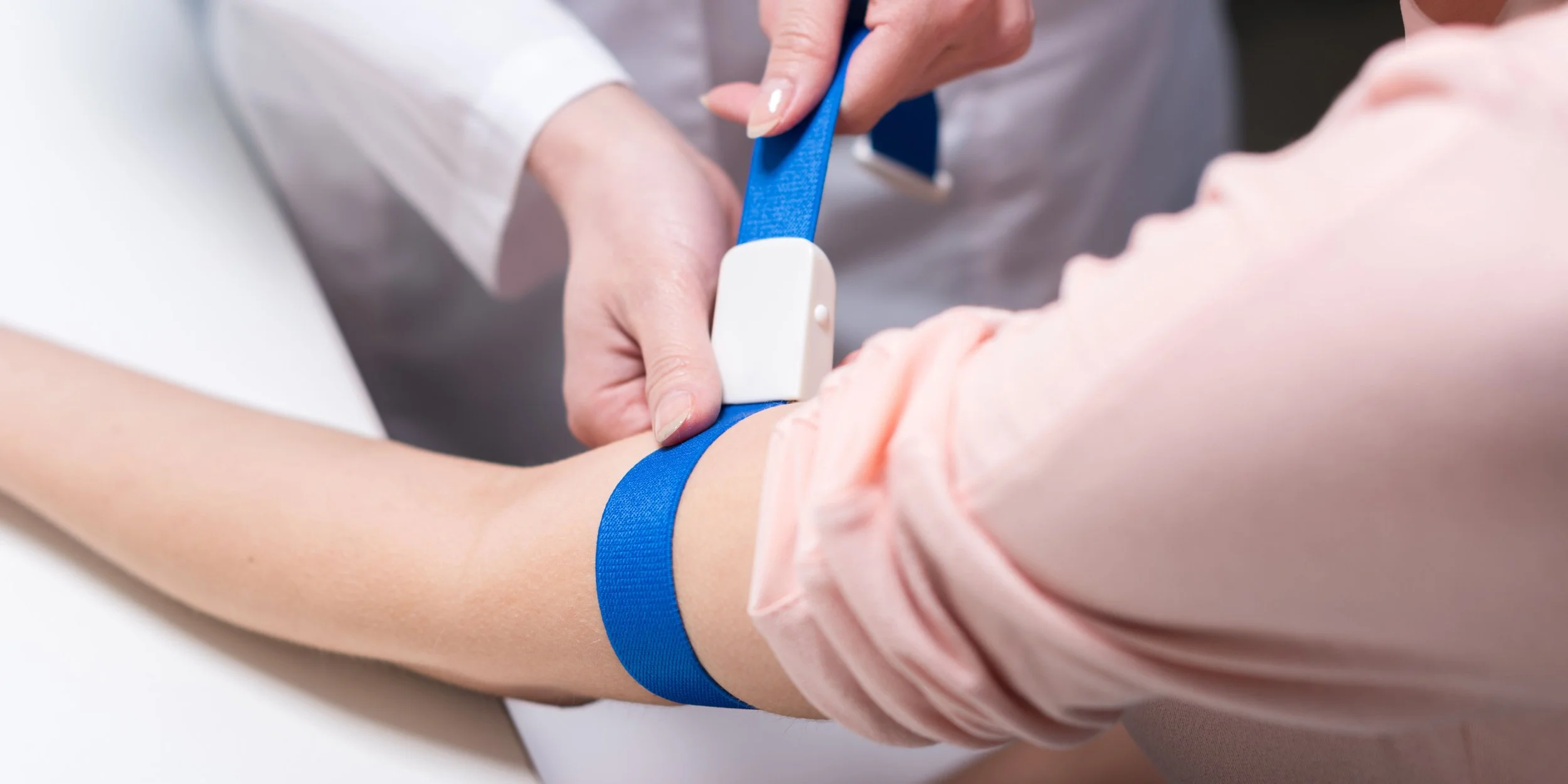 A healthcare professional is applying a blue tourniquet to a patient's arm before drawing blood or administering an injection.