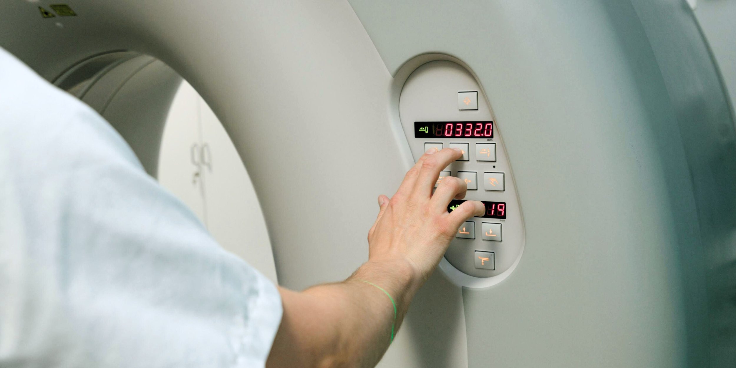 A person’s hand pressing buttons on a medical imaging machine control panel.
