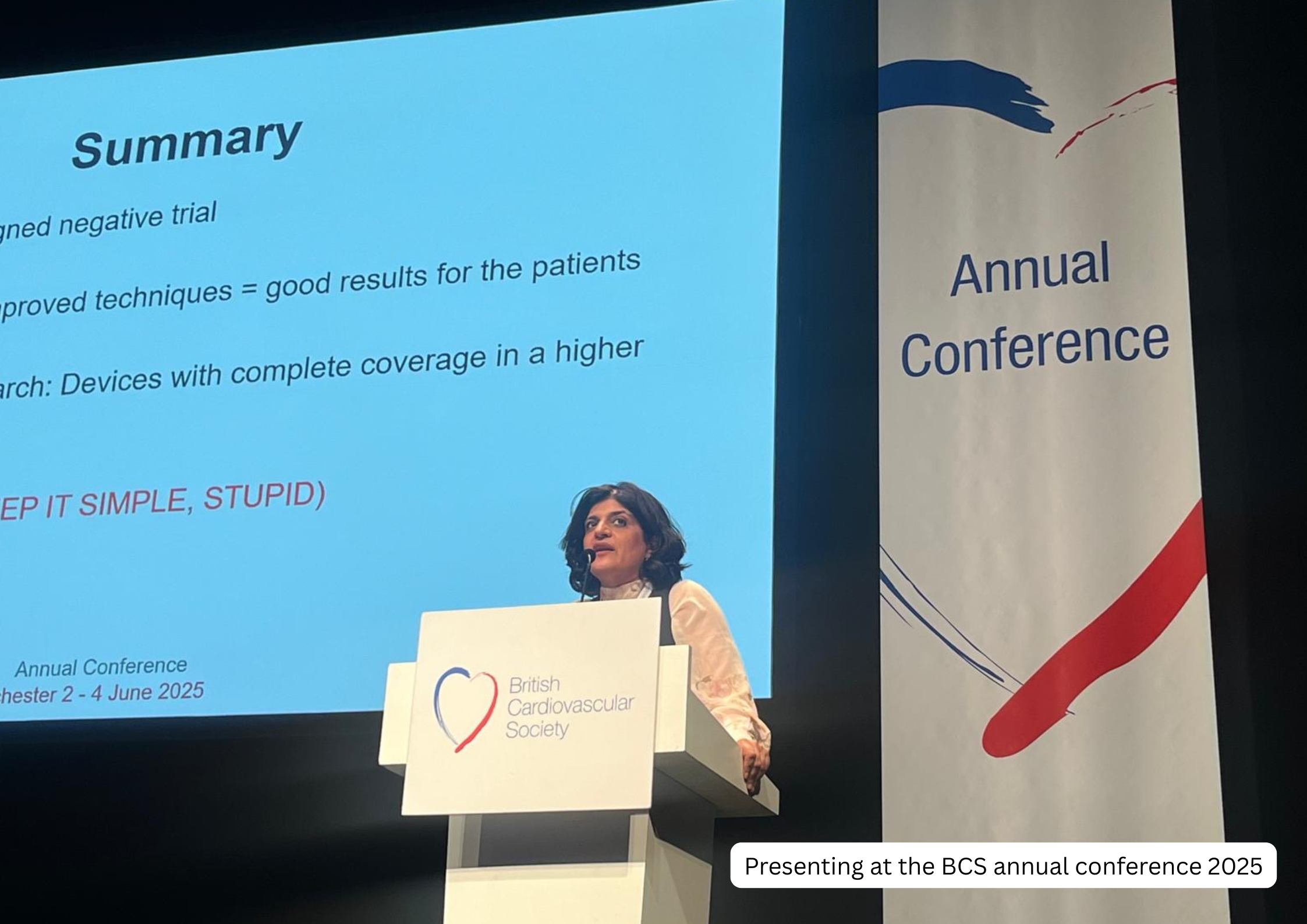 A woman presenting at the British Cardiovascular Society (BCS) annual conference 2025, standing at a podium with a logo, in front of a large screen displaying a summary slide with text about research results.