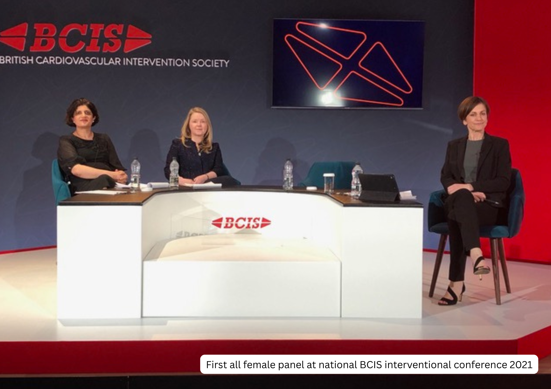 First all female panel at national BCIS interventional conference 2021 with three women seated at a table with water bottles, a monitor displaying geometric shapes, and a backdrop with BCIS logo and text.