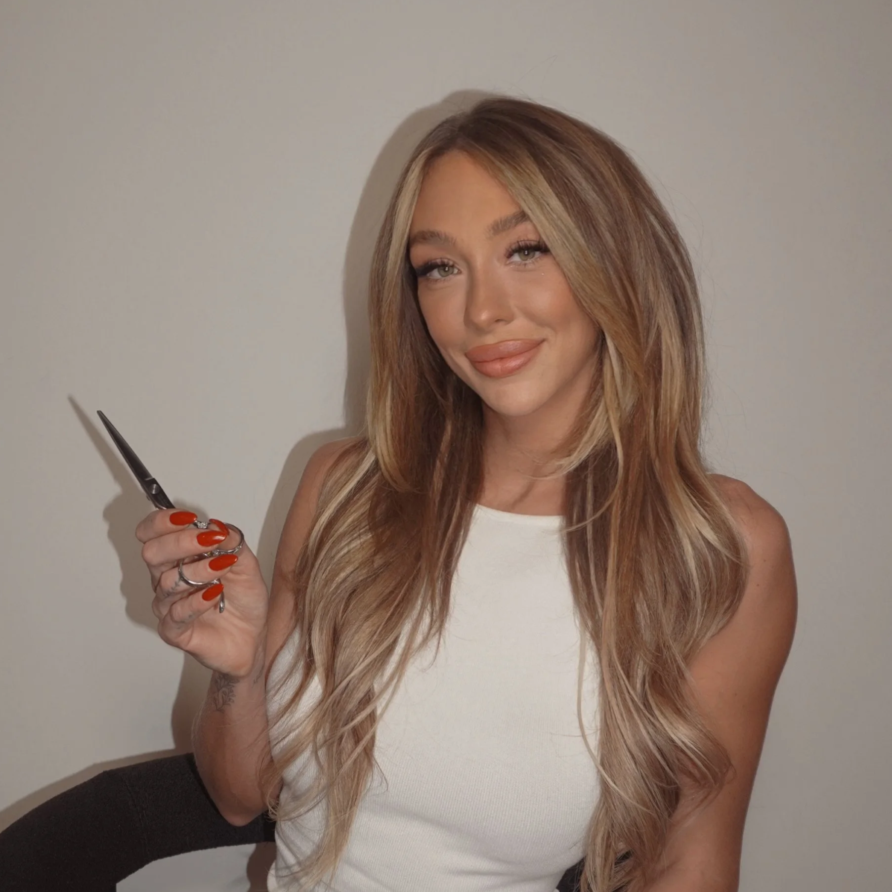 Woman with long blonde hair in a brown corset top and leather pants sitting on a chair.