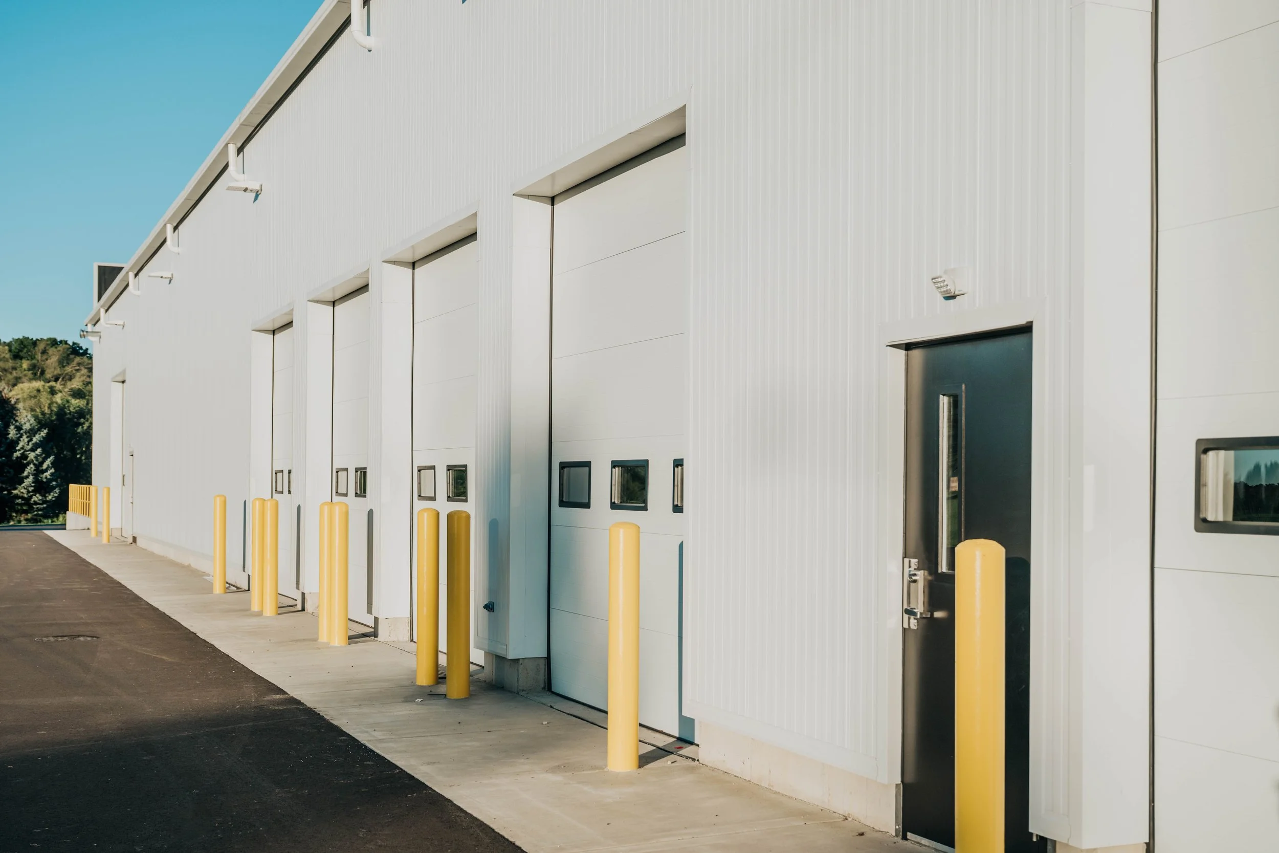 Overhead doors protected by yellow bollards along the insulated metal panel exterior of the Weller Auto addition