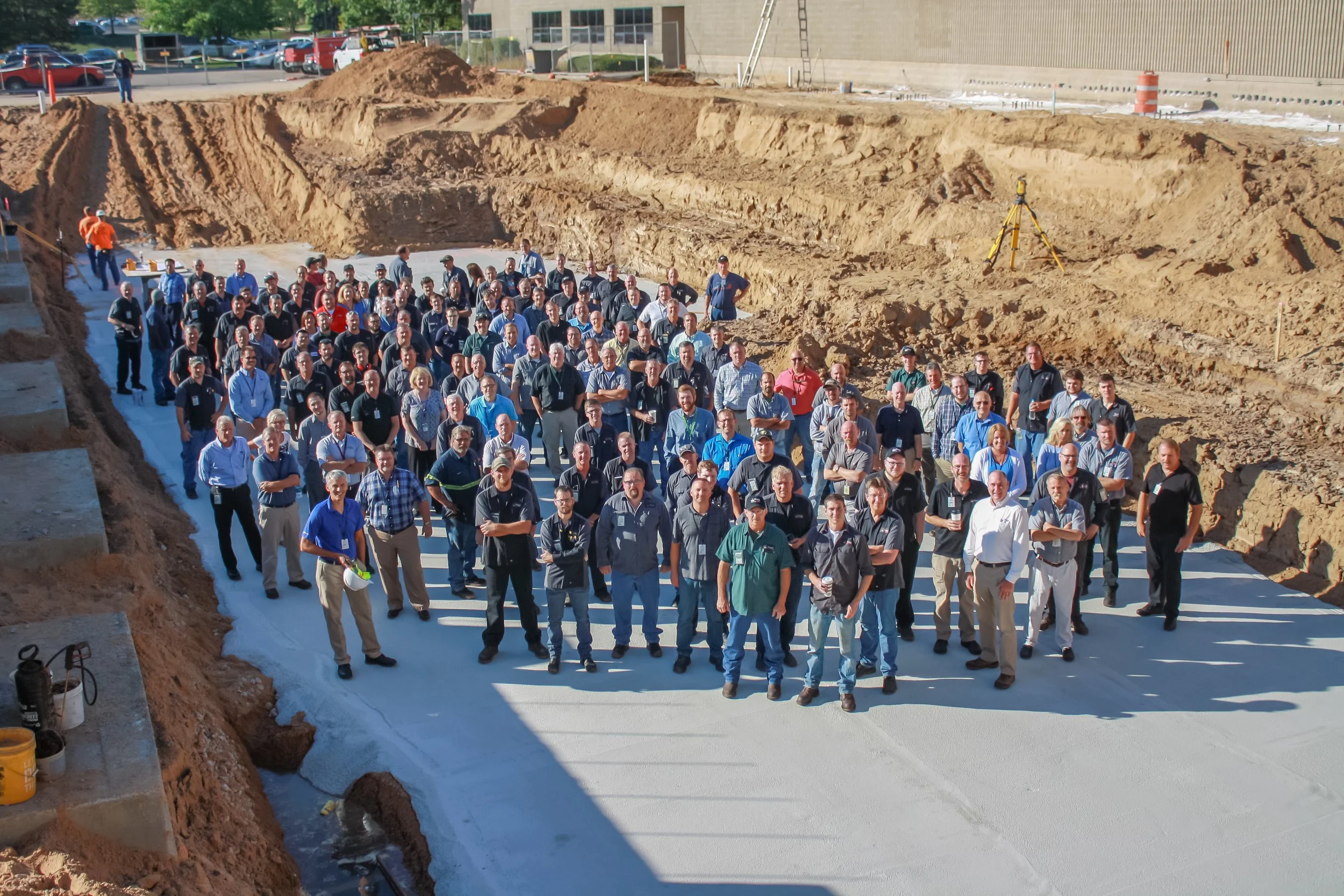 Group of construction workers and professionals standing on a freshly poured concrete foundation at a construction site.