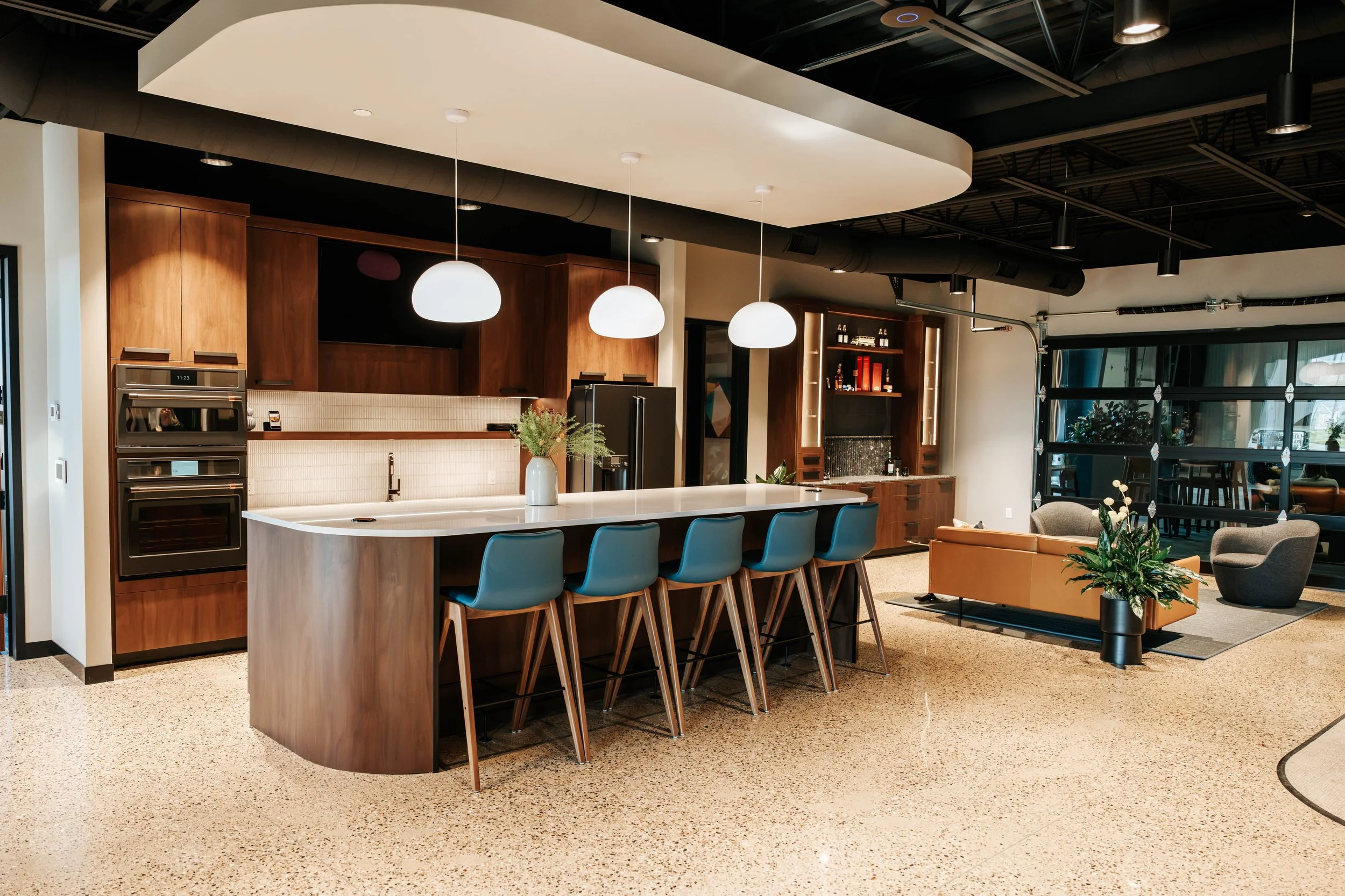 Office kitchen at PDM Properties with a curved walnut island, blue barstools and pendant lights.