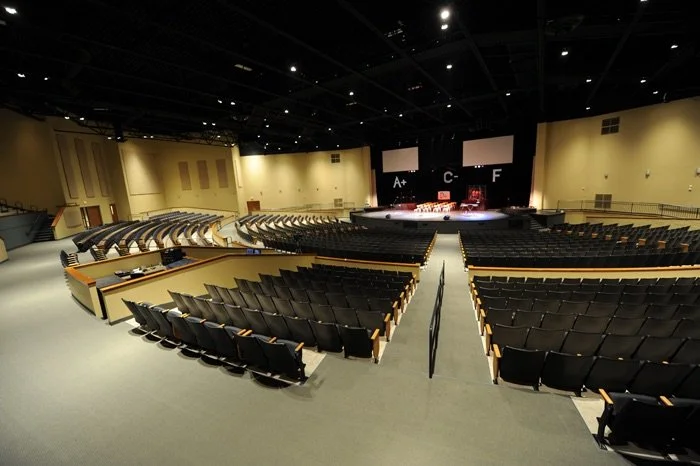 Empty auditorium with tiered seating facing a stage with two large screens showing grade letters.