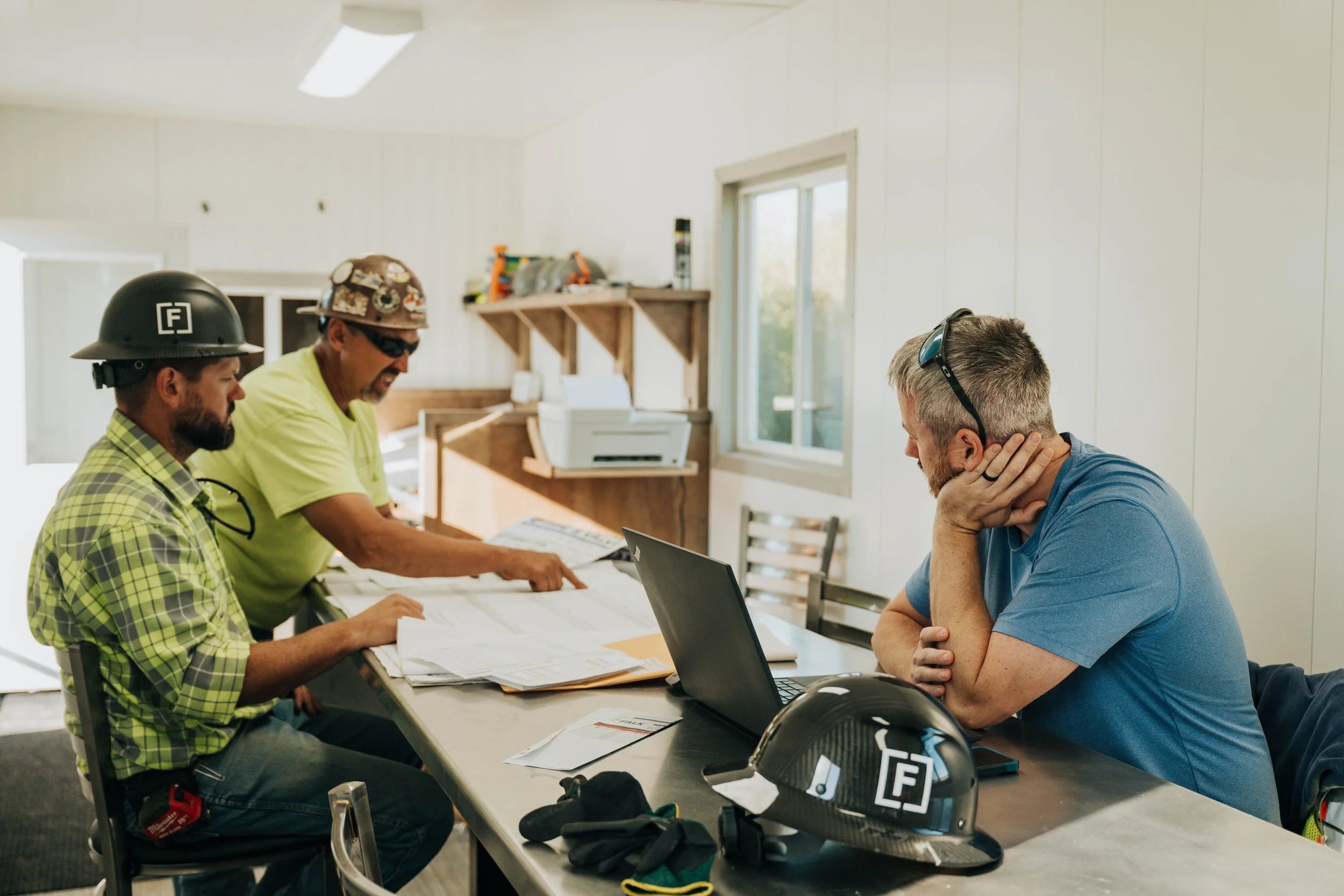 Three FCC Construction team members review project drawings together at a table in the jobsite trailer.
